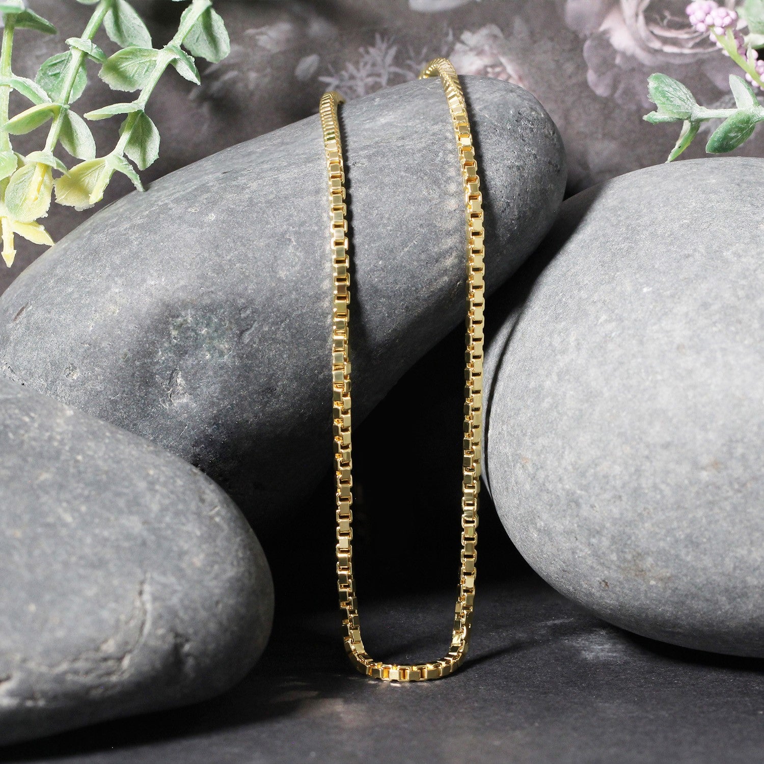 14k yellow gold semi-solid box chain draped over smooth grey stones.
