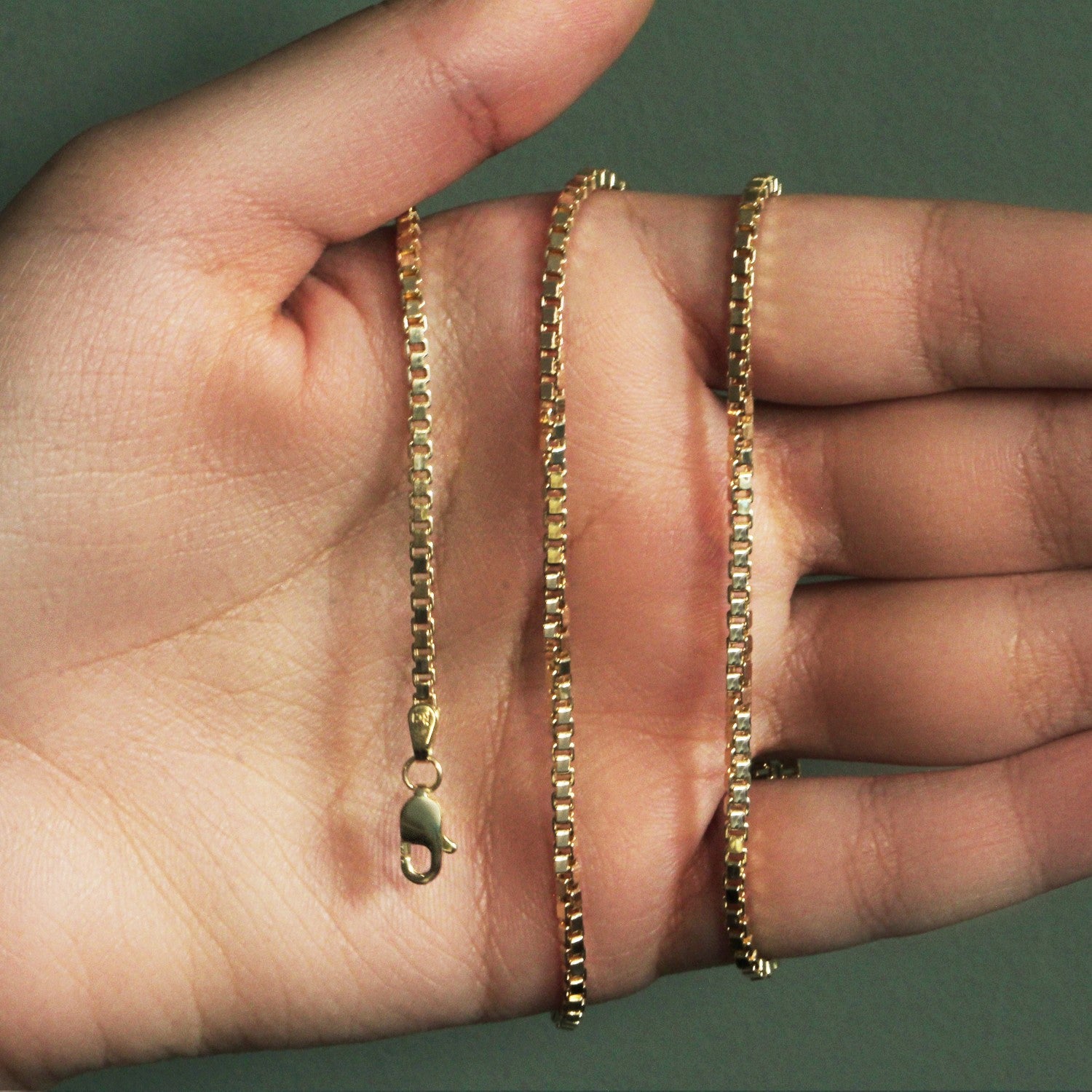 A 14k yellow gold semi-solid box chain with a lobster clasp held in a hand.