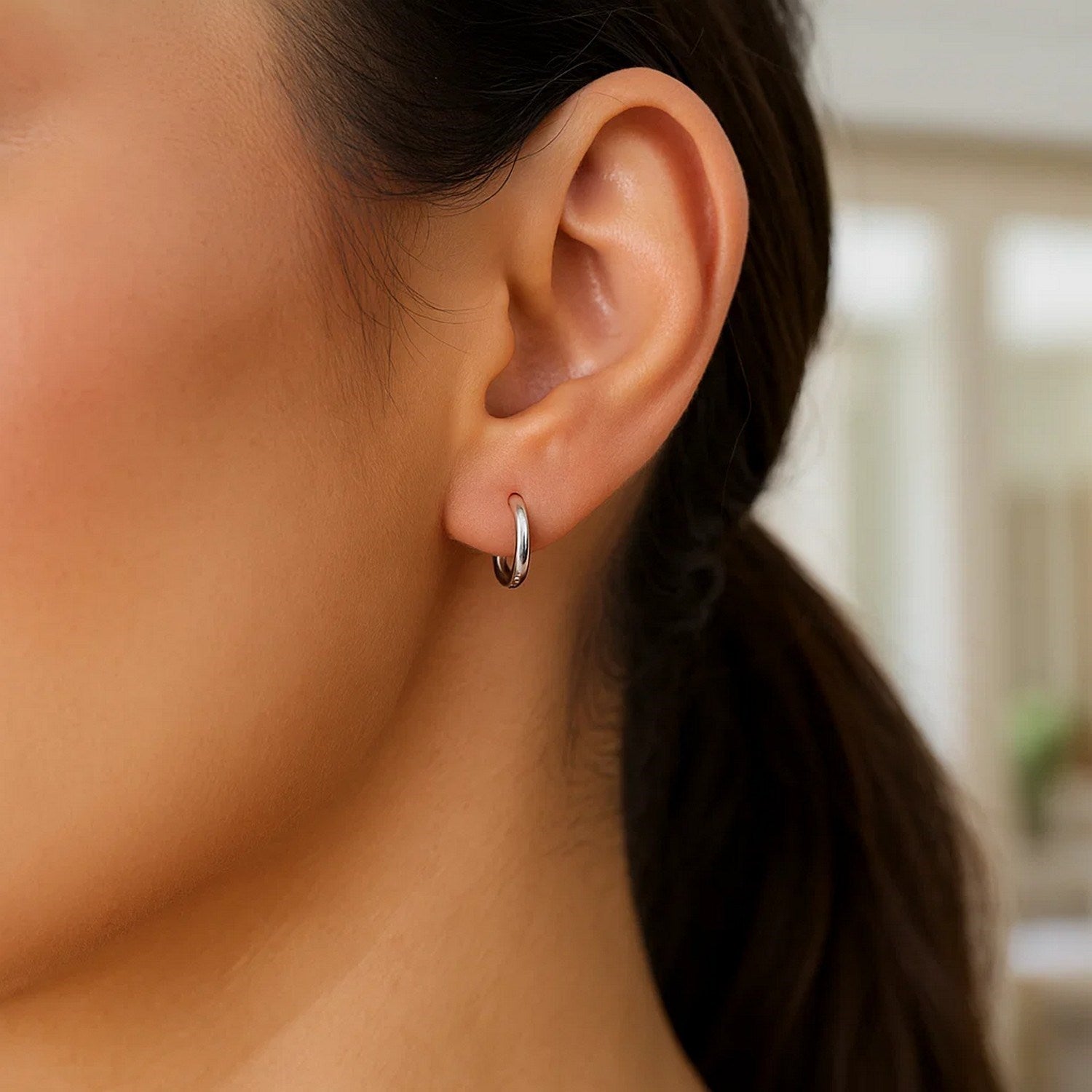 Sterling silver rhodium plated thin and small polished hoop earrings on an ear.
