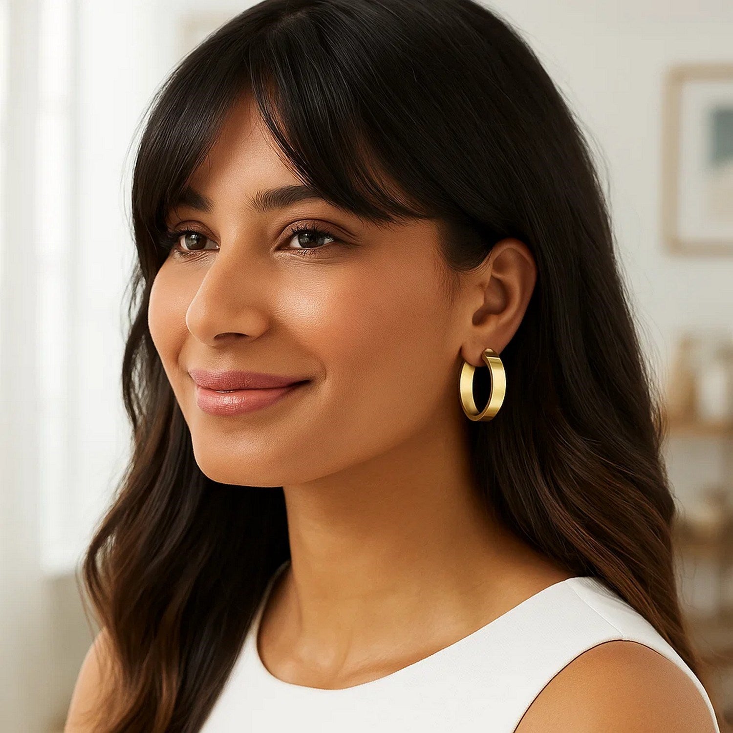 Medium tube shaped hoop earrings in 14K yellow gold on a woman.