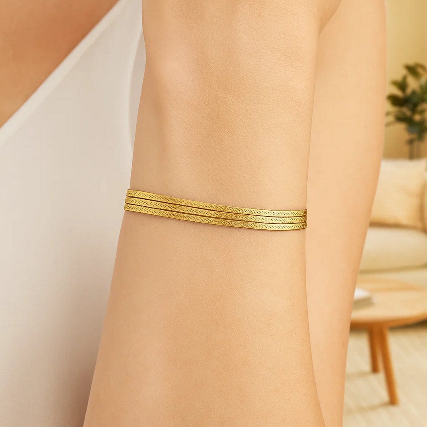 A 14k yellow gold three-strand herringbone chain bracelet on a person's arm.