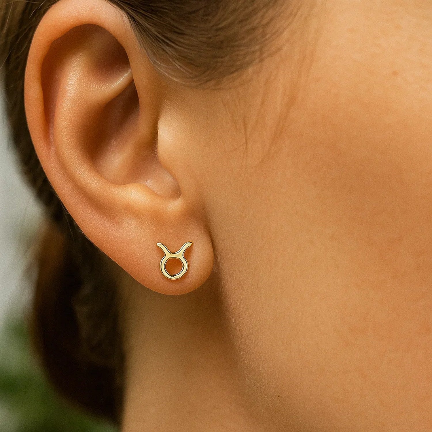 A single 14K yellow gold Taurus stud earring is worn on an ear.