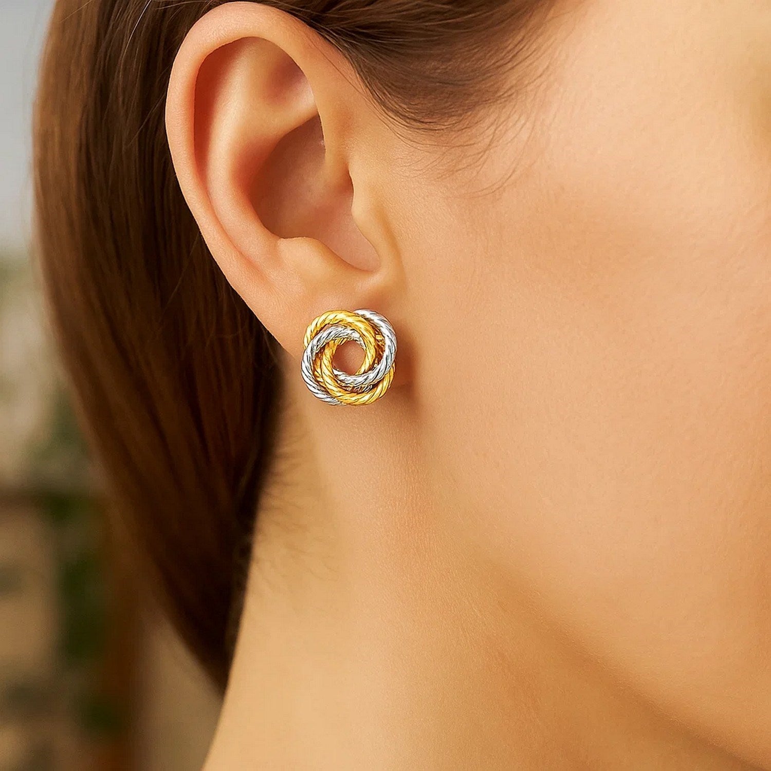 A woman wears a two-tone gold love knot earring on her right ear.
