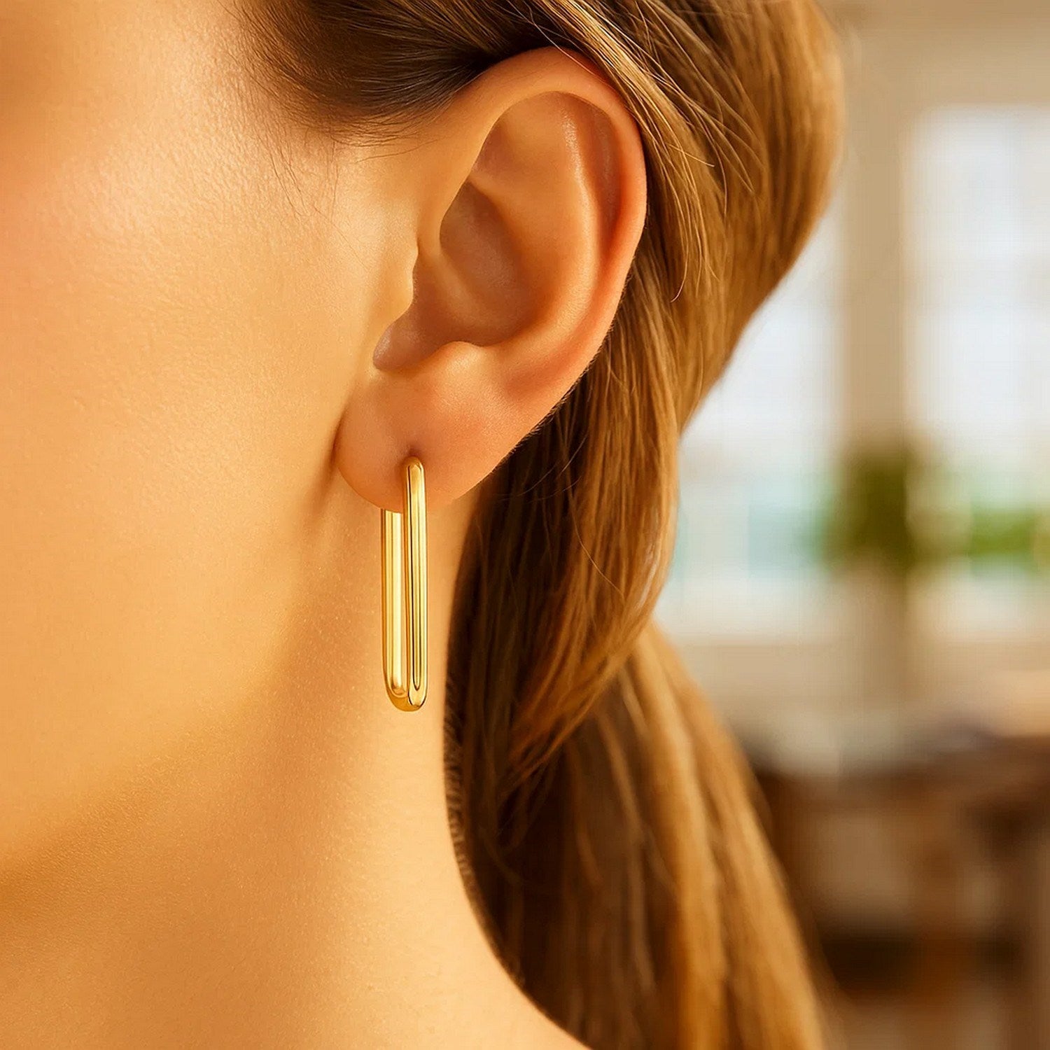 A woman wears a pair of 14k yellow gold endless rectangle hoop earrings.