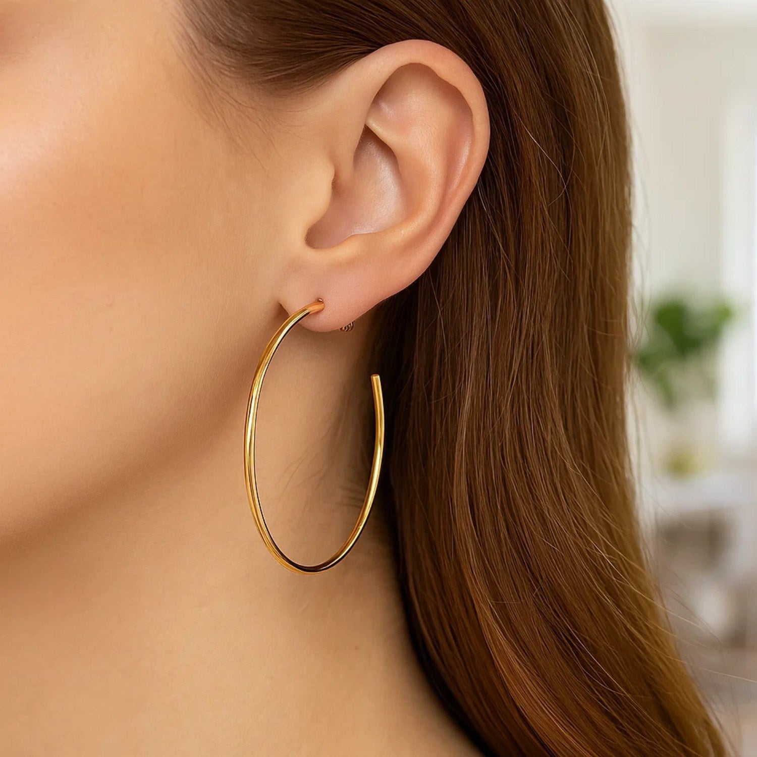 A woman wears a single polished 14k yellow gold hoop earring.