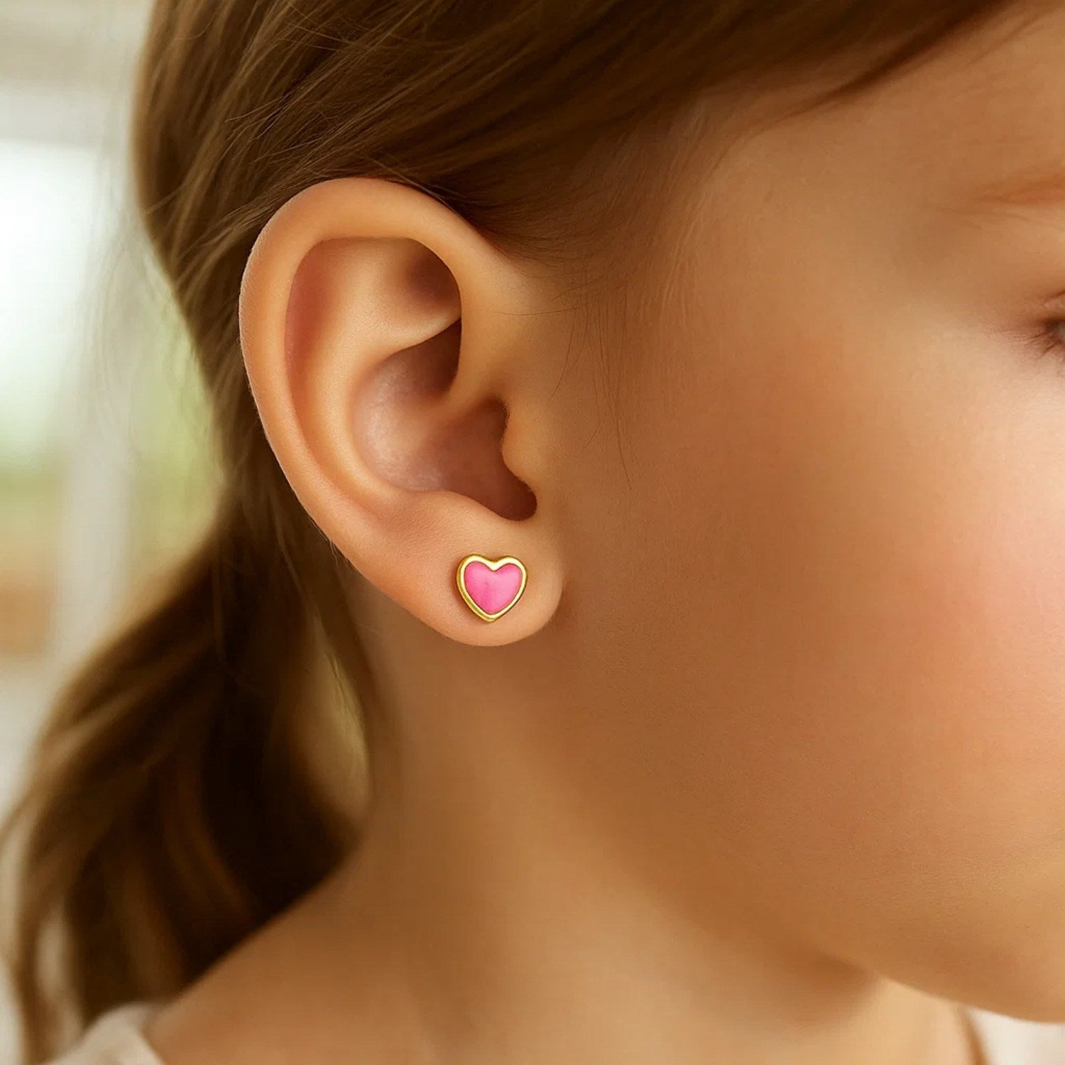 14k yellow gold and enamel pink heart stud earrings on a child's ear.