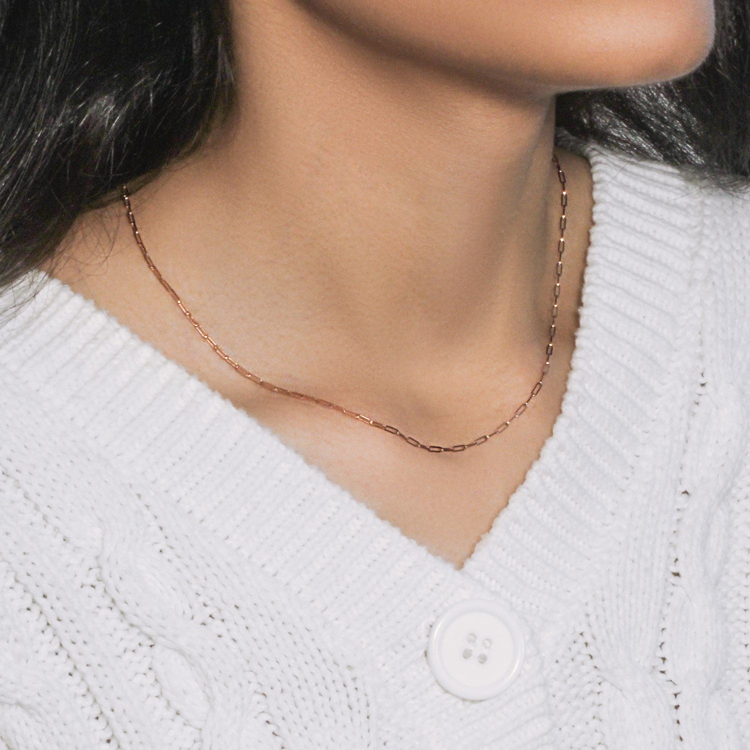A 14K rose gold paperclip chain necklace is worn on a person's neck over a white sweater.