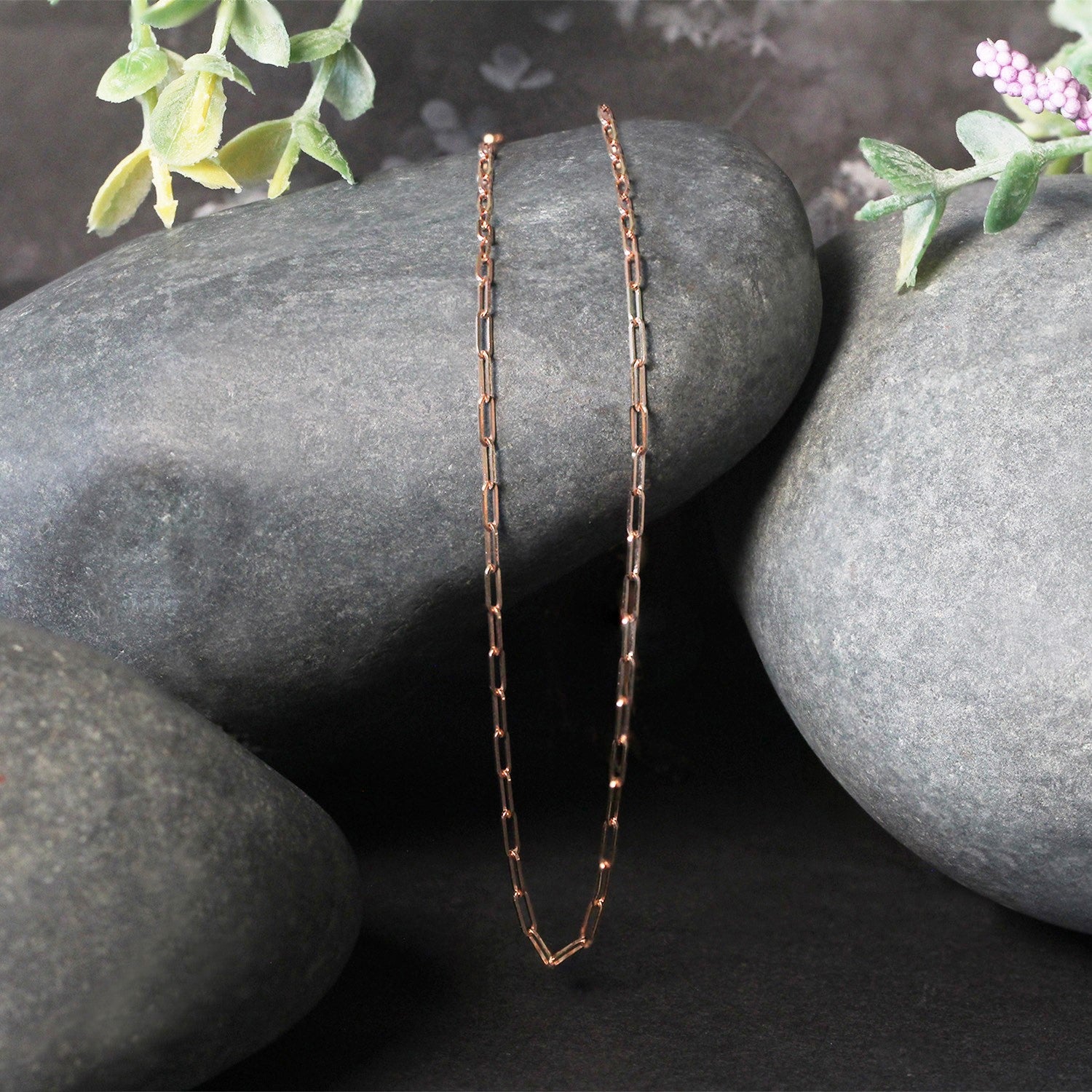 14K rose gold fine paperclip chain with 1.50 mm links on dark grey rocks.