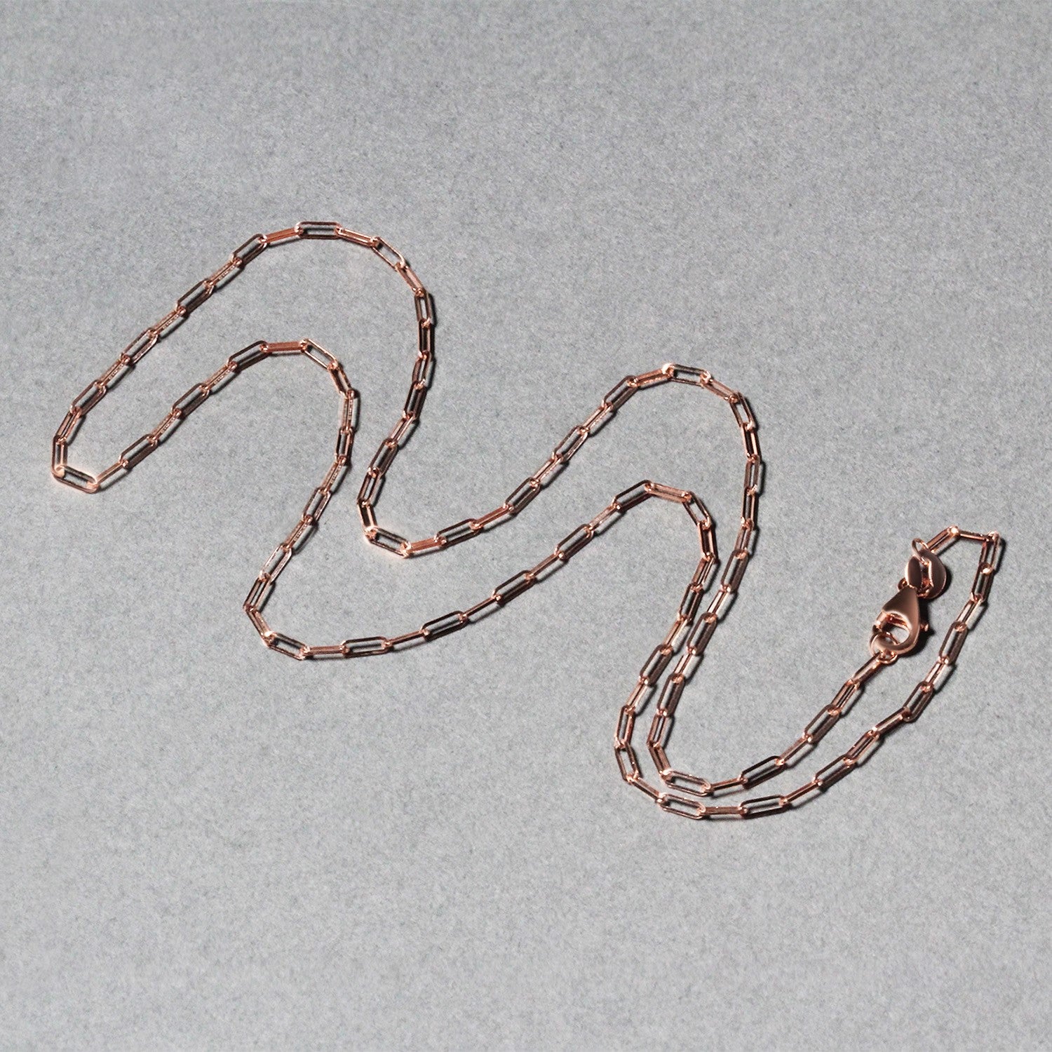 14K rose gold fine paperclip chain with a lobster clasp on a gray background.