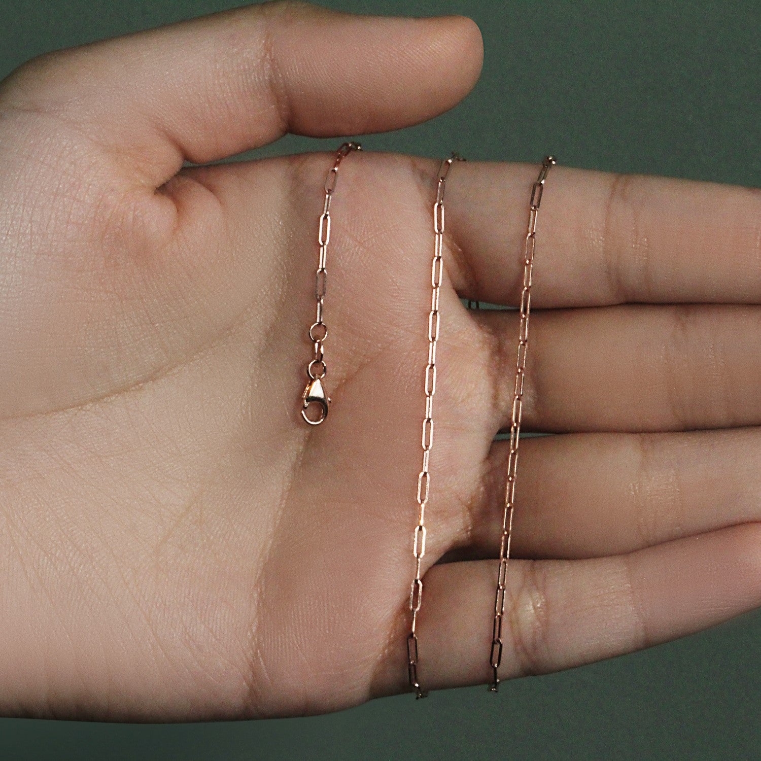 14K rose gold fine paperclip chain with a lobster clasp held in a hand.