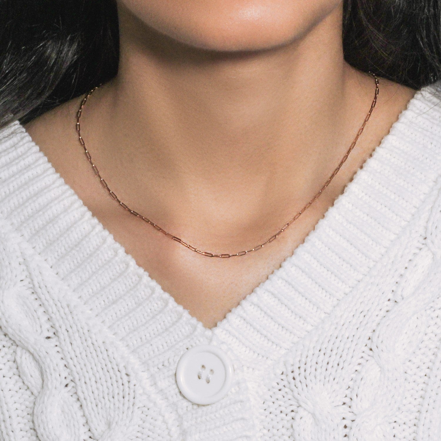 A 14K rose gold paperclip chain necklace on a person wearing a white cable-knit sweater.