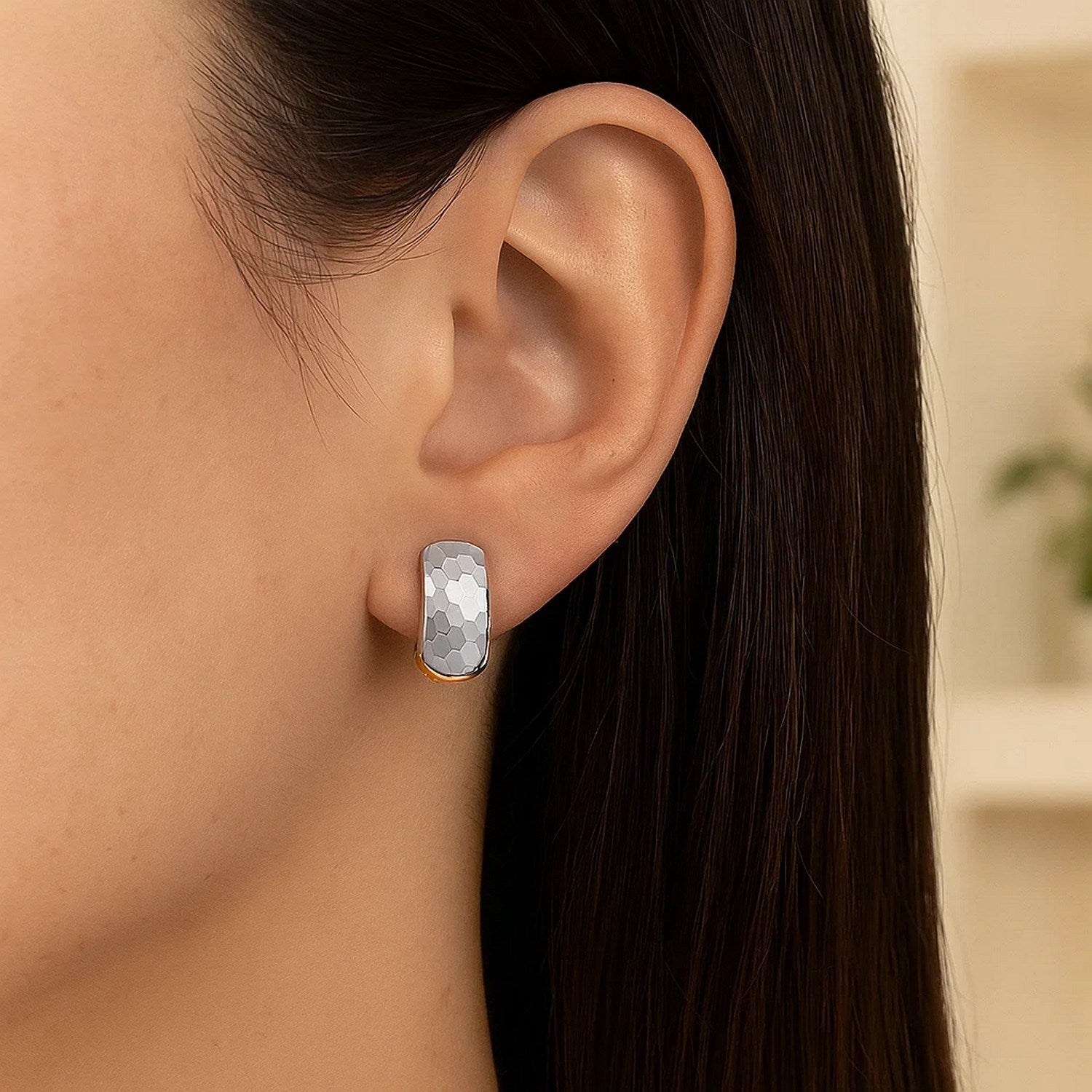 A two-tone gold hoop earring with a diamond-cut, interlaced style on a woman's ear.