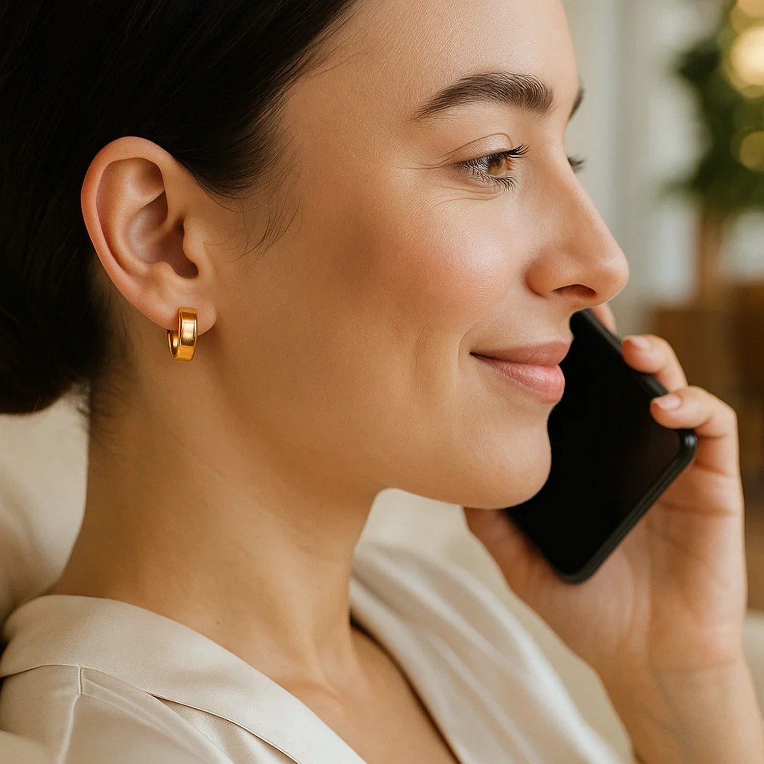 Small tube-shaped hoop earrings in 14K yellow gold on a woman's ear.