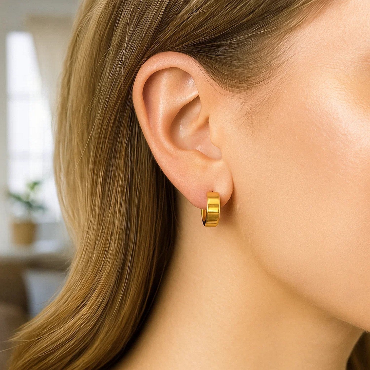 Small tube-shaped hoop earrings in 14K yellow gold on a woman's ear.
