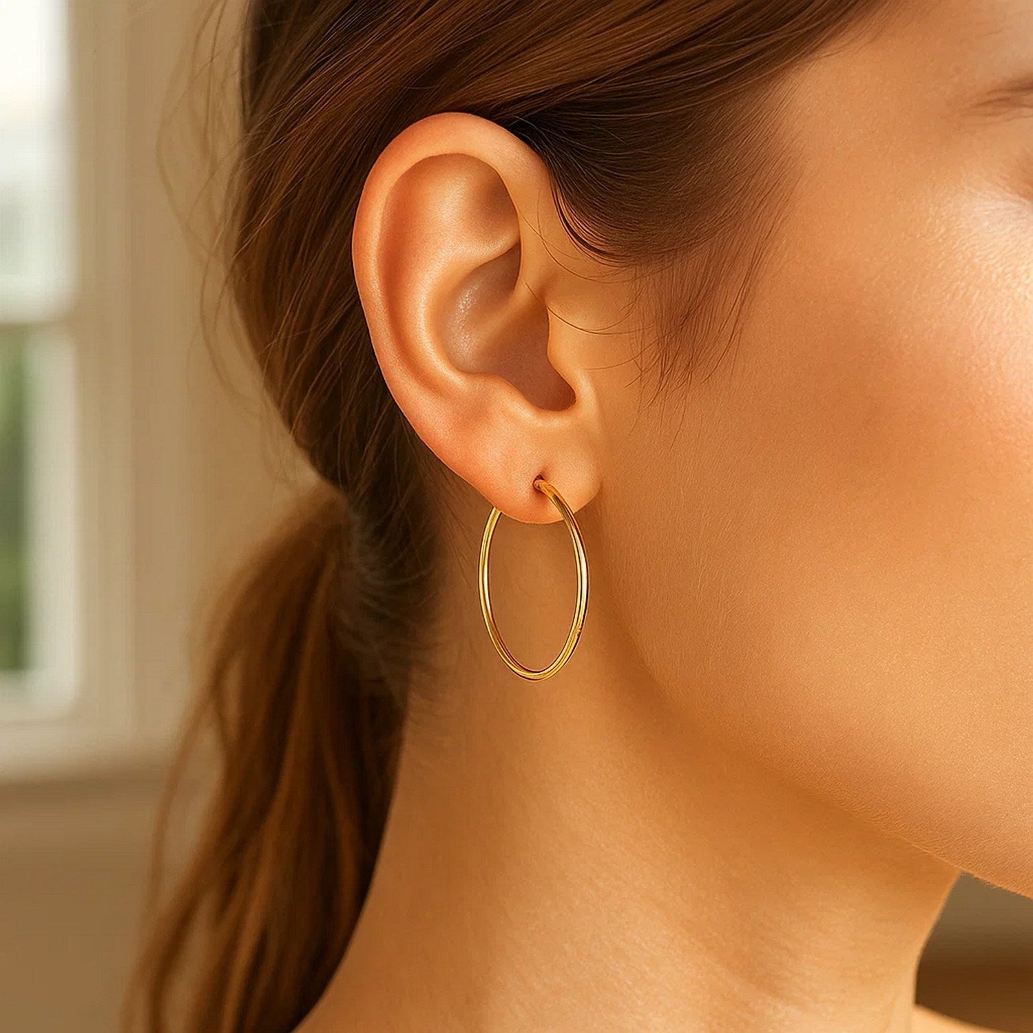 A woman wears a single polished 10k yellow gold hoop earring.