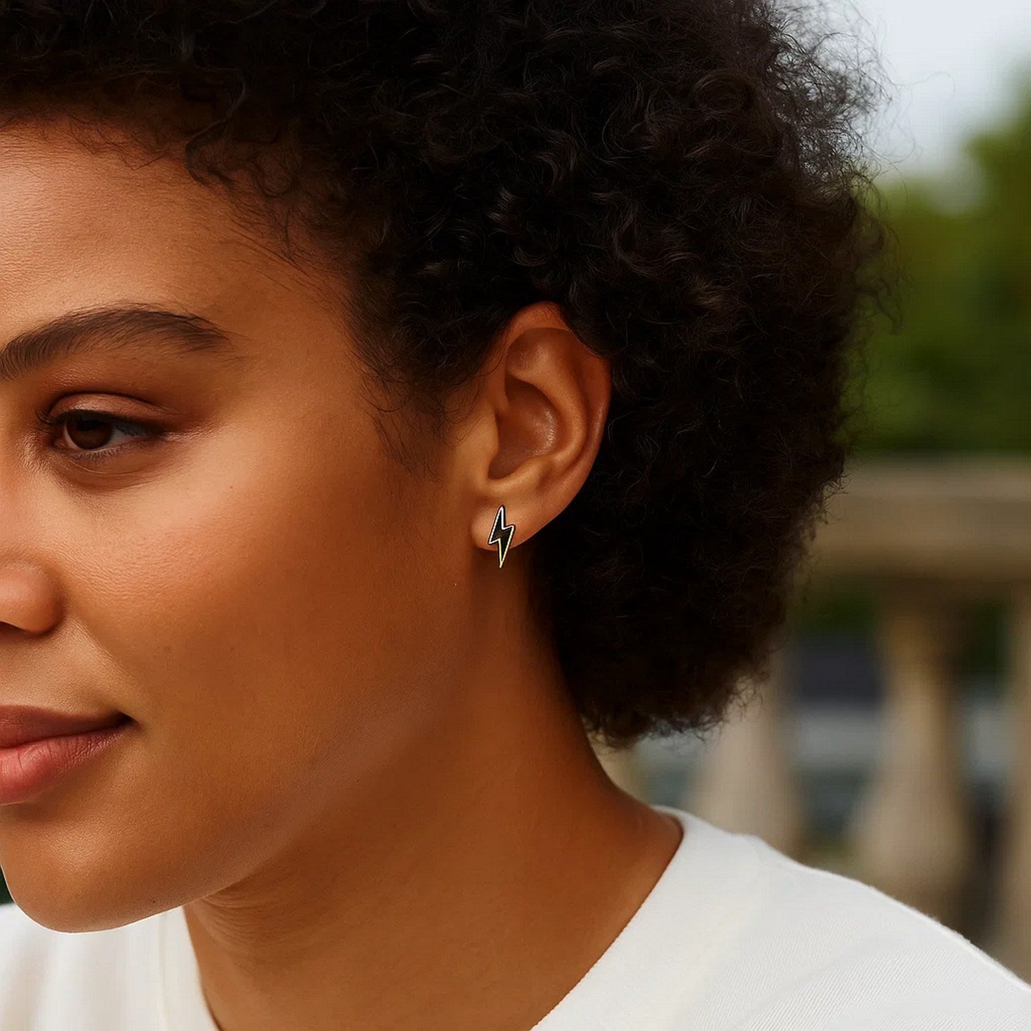 14k yellow gold and enamel black lightning bolt stud earrings on a woman's ear.