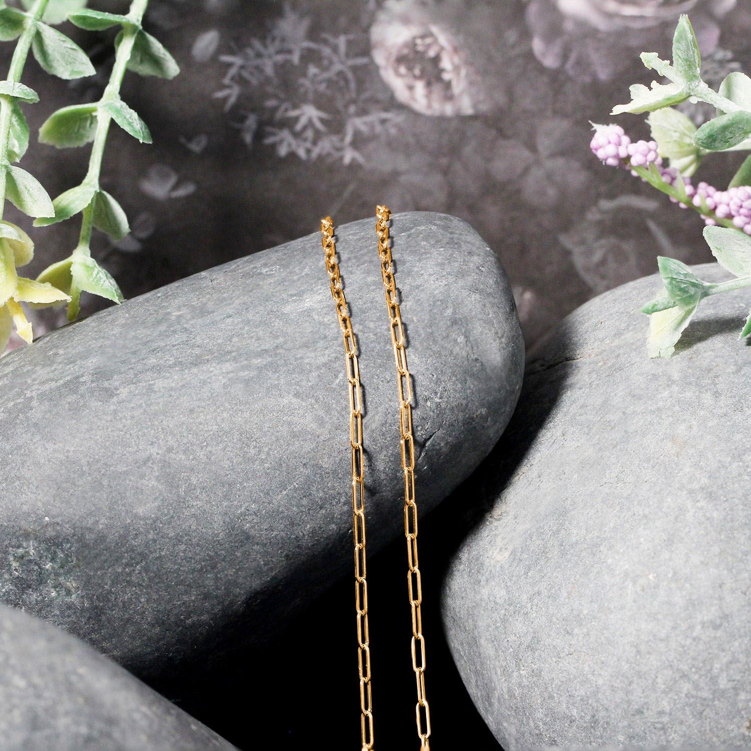 A 14k yellow gold adjustable paperclip chain rests on gray stones.