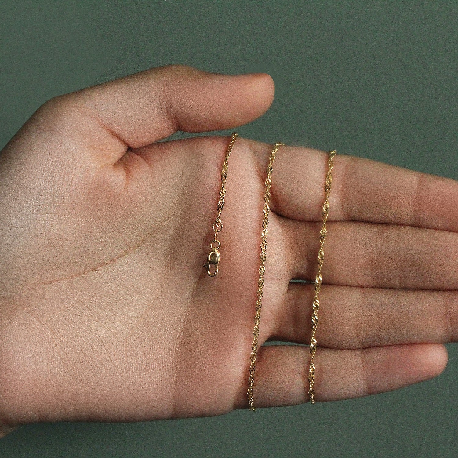 14k yellow gold Singapore chain with a lobster clasp held in an open hand.