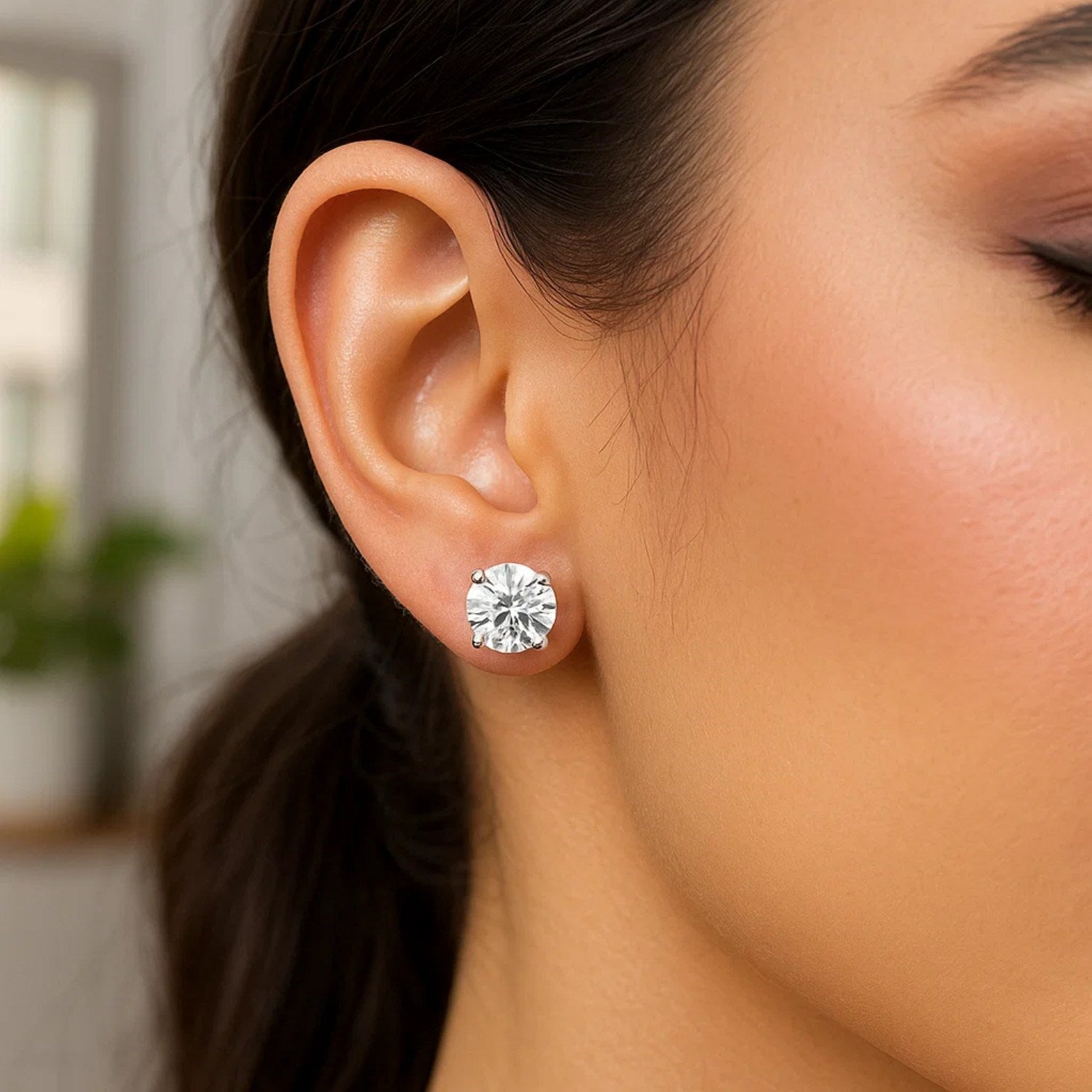 Sterling silver round CZ stud earrings with a four-prong setting on a woman's ear.
