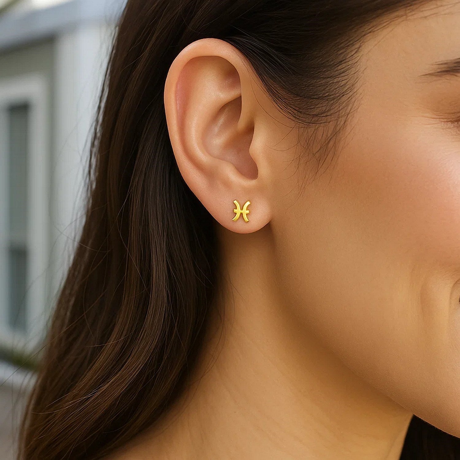 A woman wears a single 14K yellow gold Pisces stud earring.