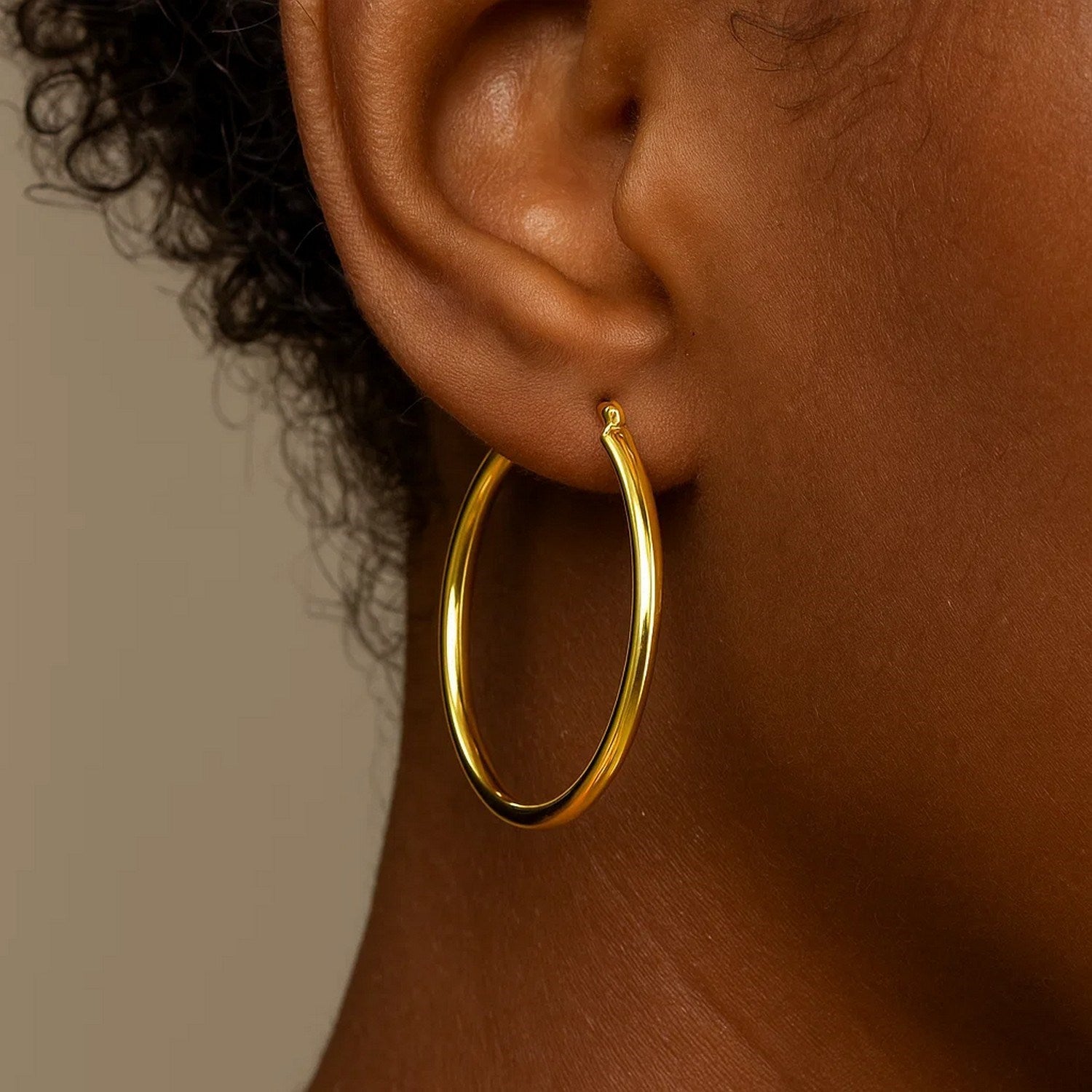 A single 10k yellow gold polished hoop earring is worn on an ear.