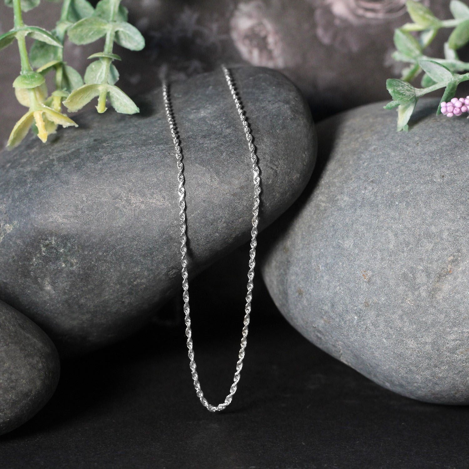 A 10k white gold solid diamond cut rope chain is draped over smooth gray rocks.