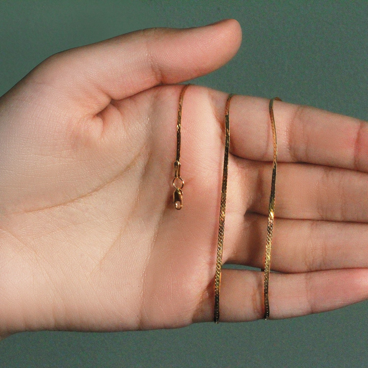 A 14k yellow gold super flex herringbone chain with a lobster clasp held in a hand.