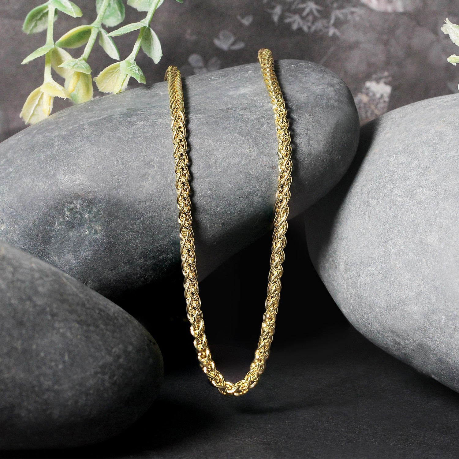 A 14k yellow gold light weight wheat chain is draped over smooth gray stones.