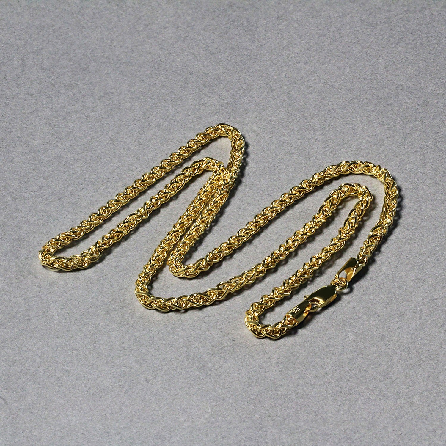 A 14k yellow gold lightweight wheat chain with a lobster clasp lies on a gray surface.