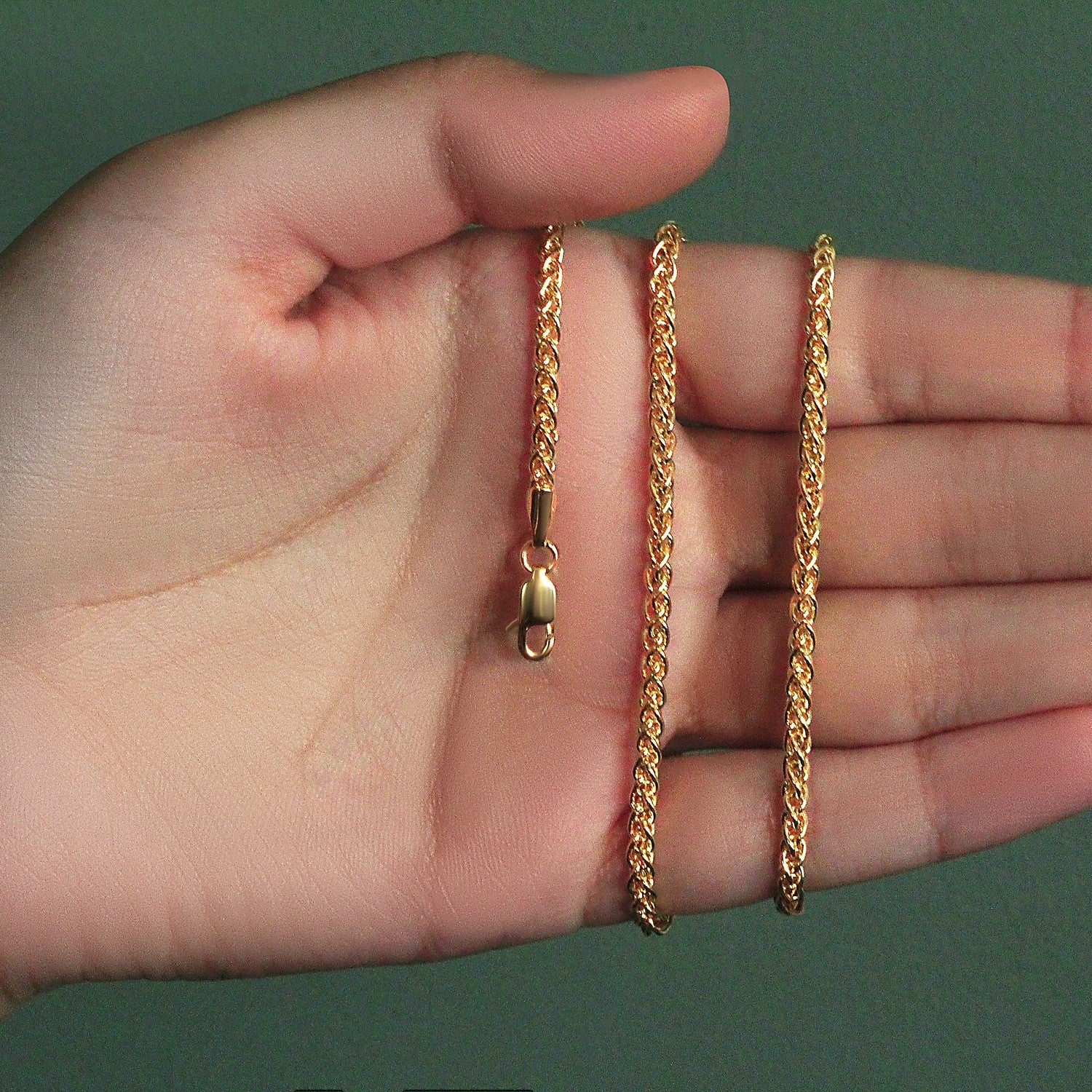 A 14k yellow gold light weight wheat chain with a lobster clasp held in a hand.