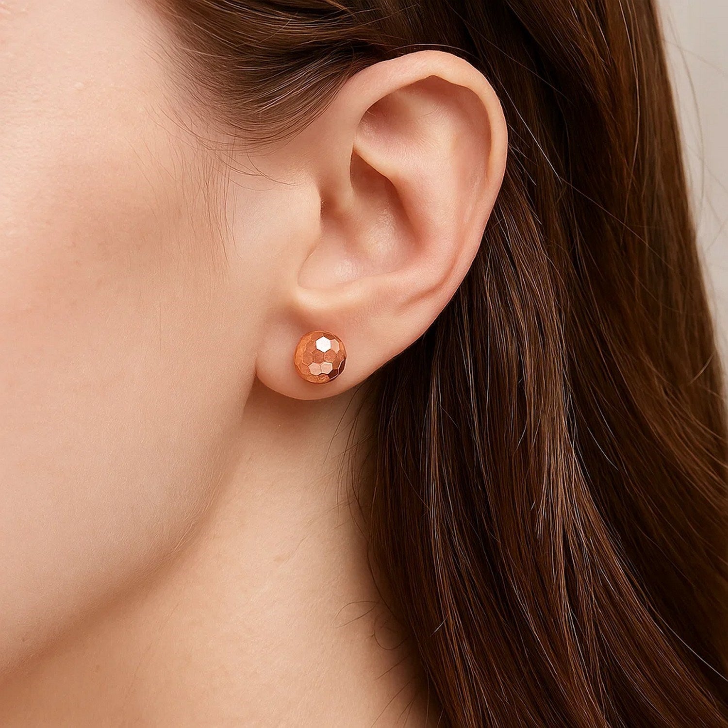 14k rose gold faceted ball earring on a woman's ear.