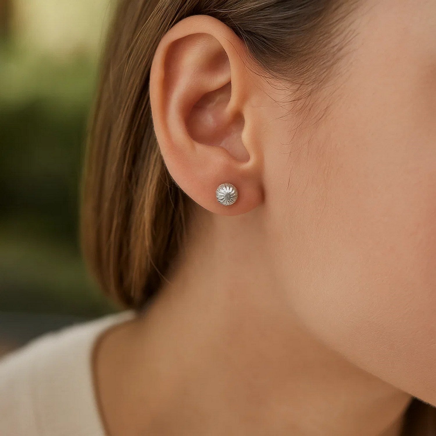A single 14K white gold ball earring with linear texture on a person's ear.