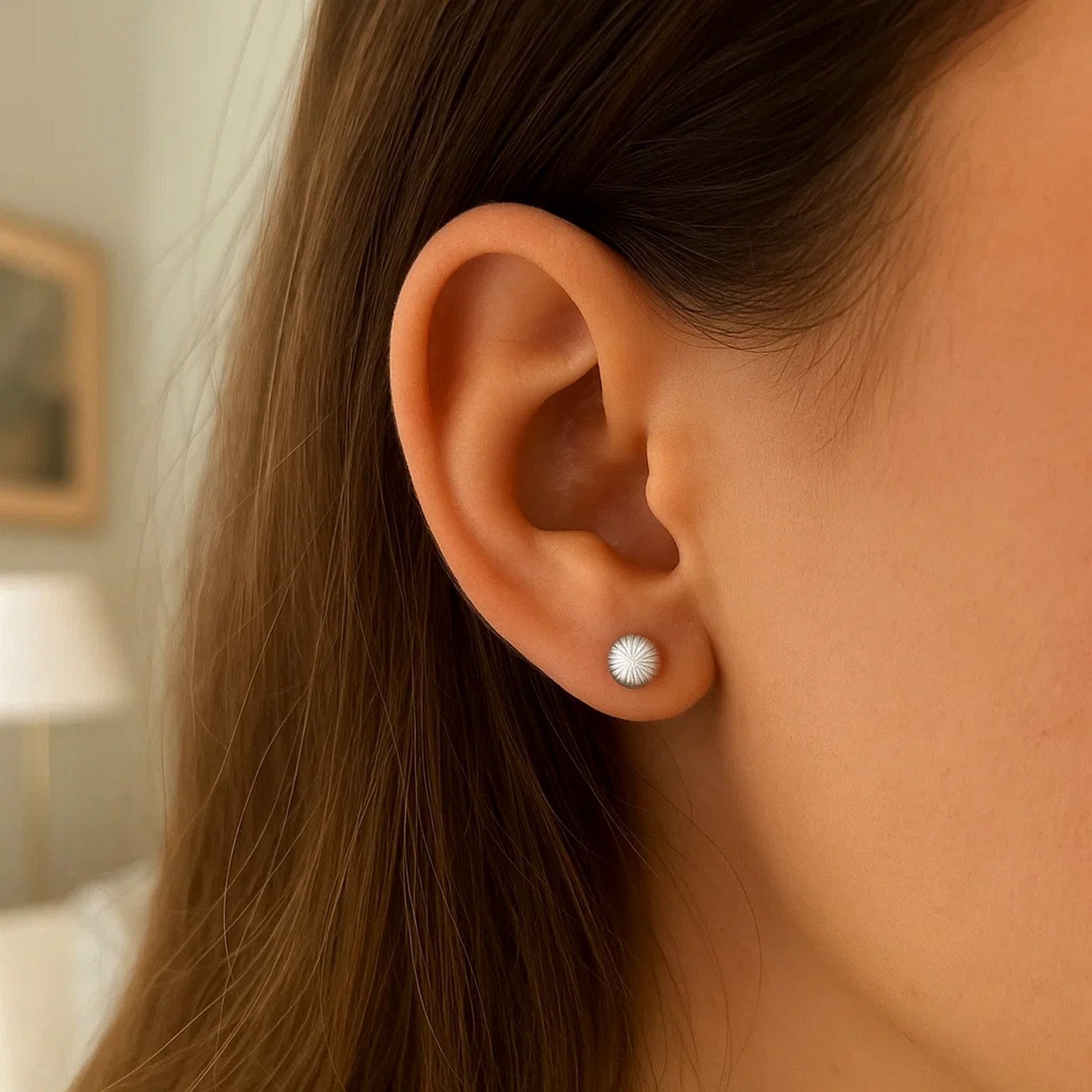 A close-up of an ear wearing a 14K white gold ball earring with linear texture.