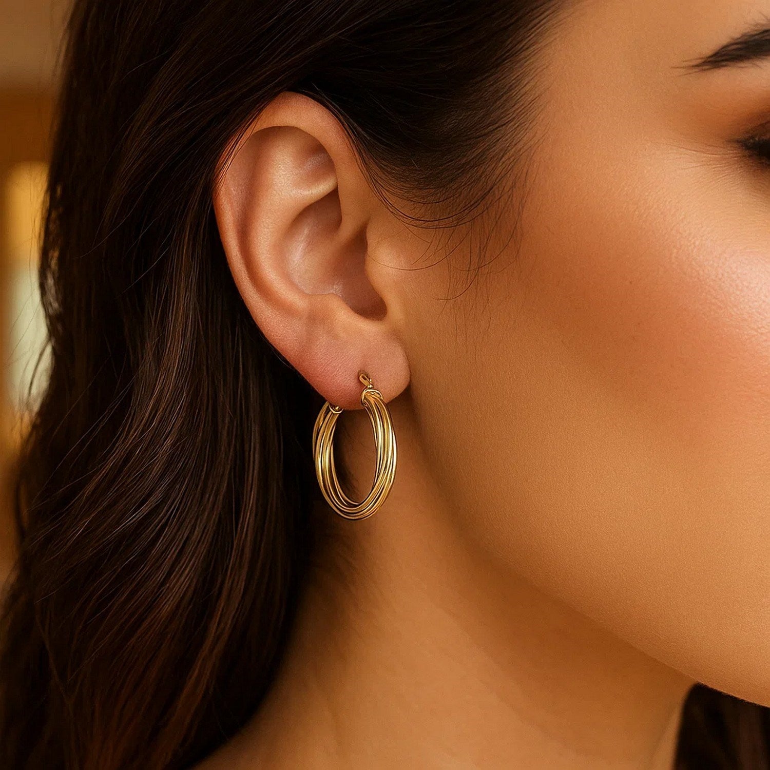 A woman wears 14K yellow gold full twist medium hoop earrings.
