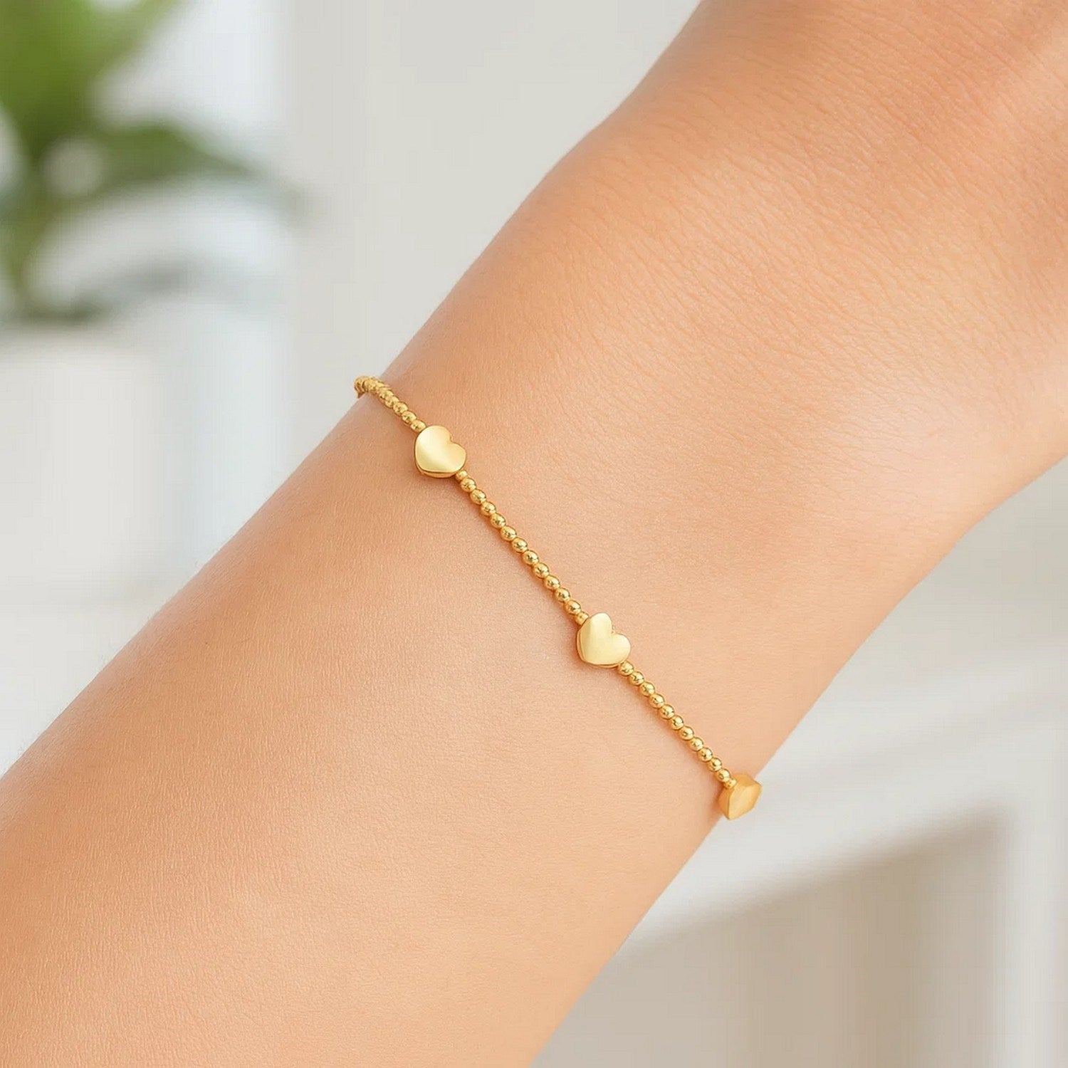 14K yellow gold bead bracelet with three heart stations on a person's wrist.
