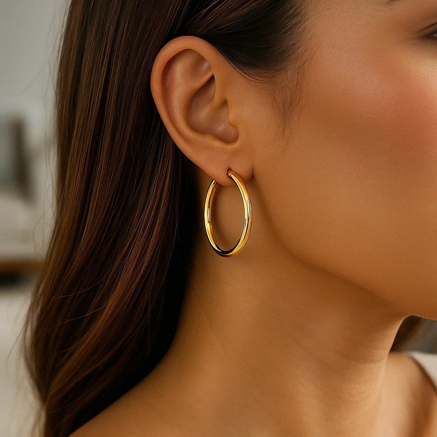 A woman wears a single polished 10k yellow gold hoop earring.