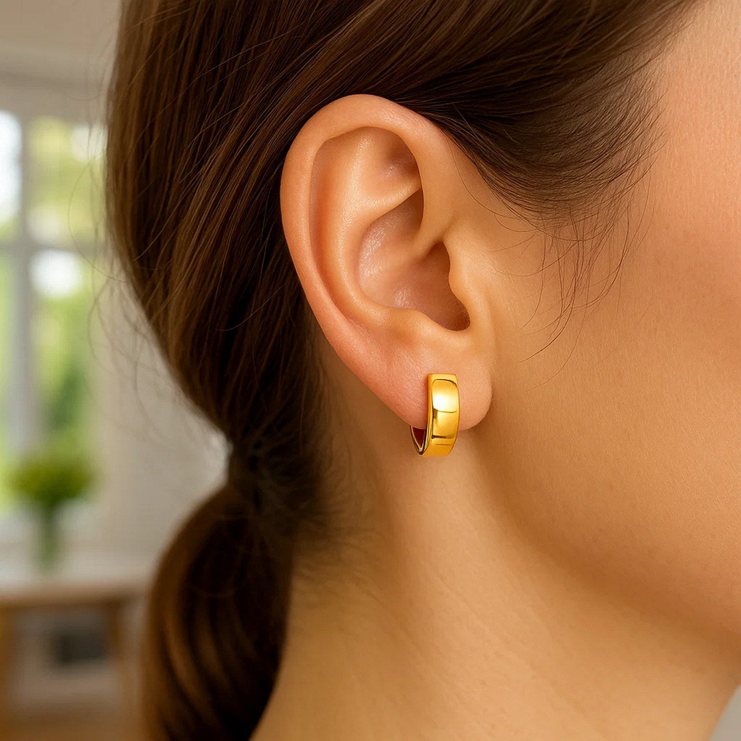 A woman wears a single 14k yellow gold snuggable hoop earring.