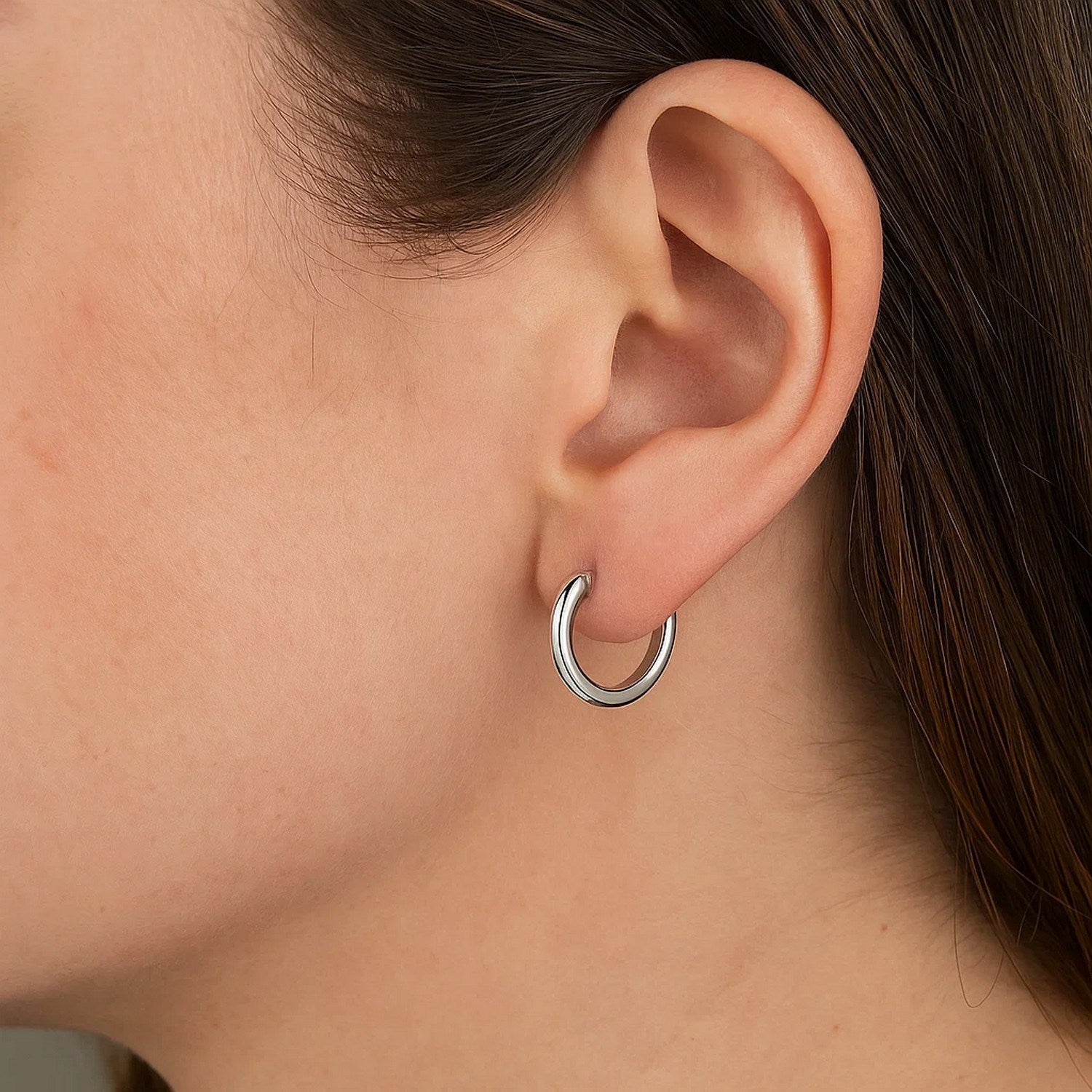 A woman wears a single polished round hoop earring made of 14k white gold.