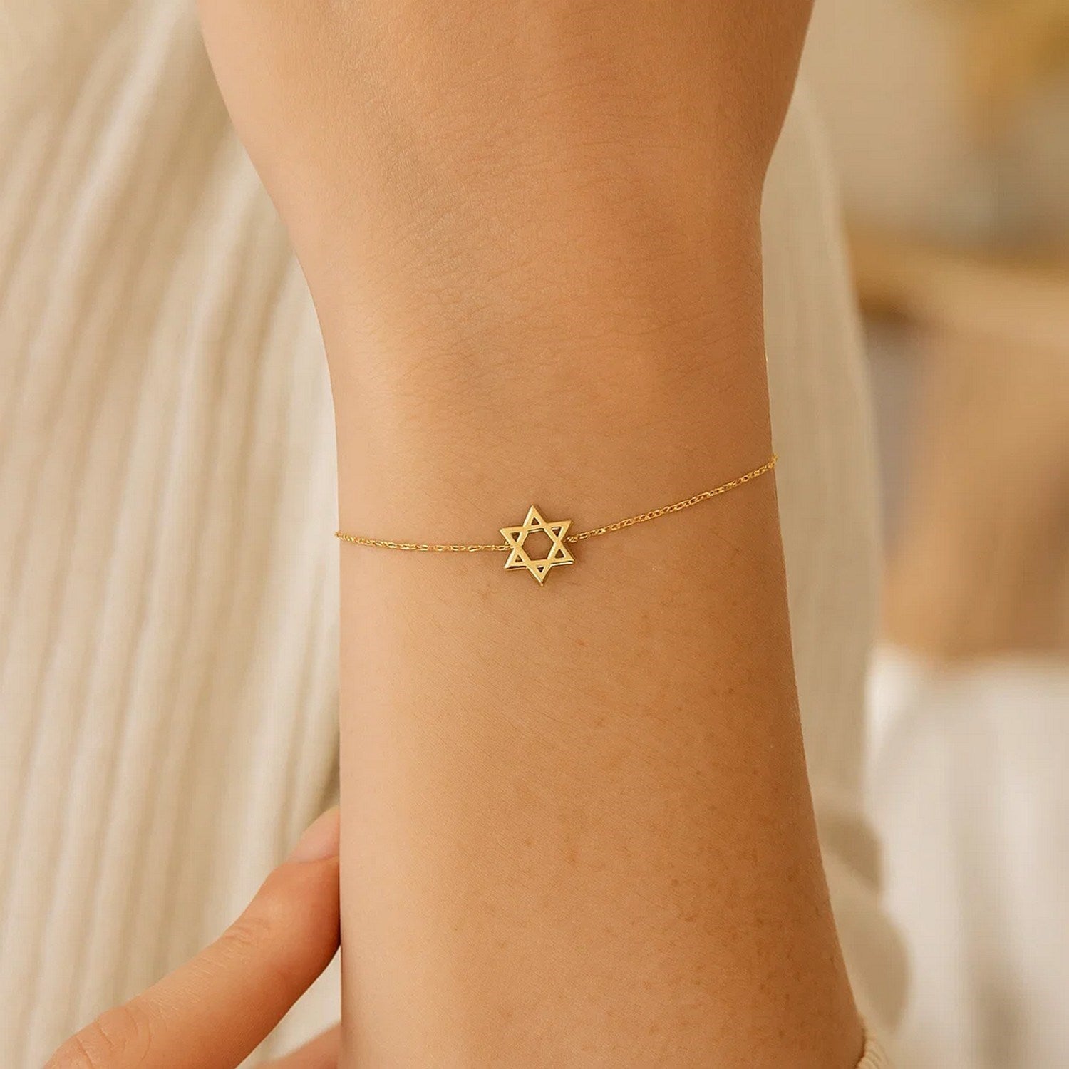 A 14k yellow gold Star of David bracelet is worn on a person's wrist.
