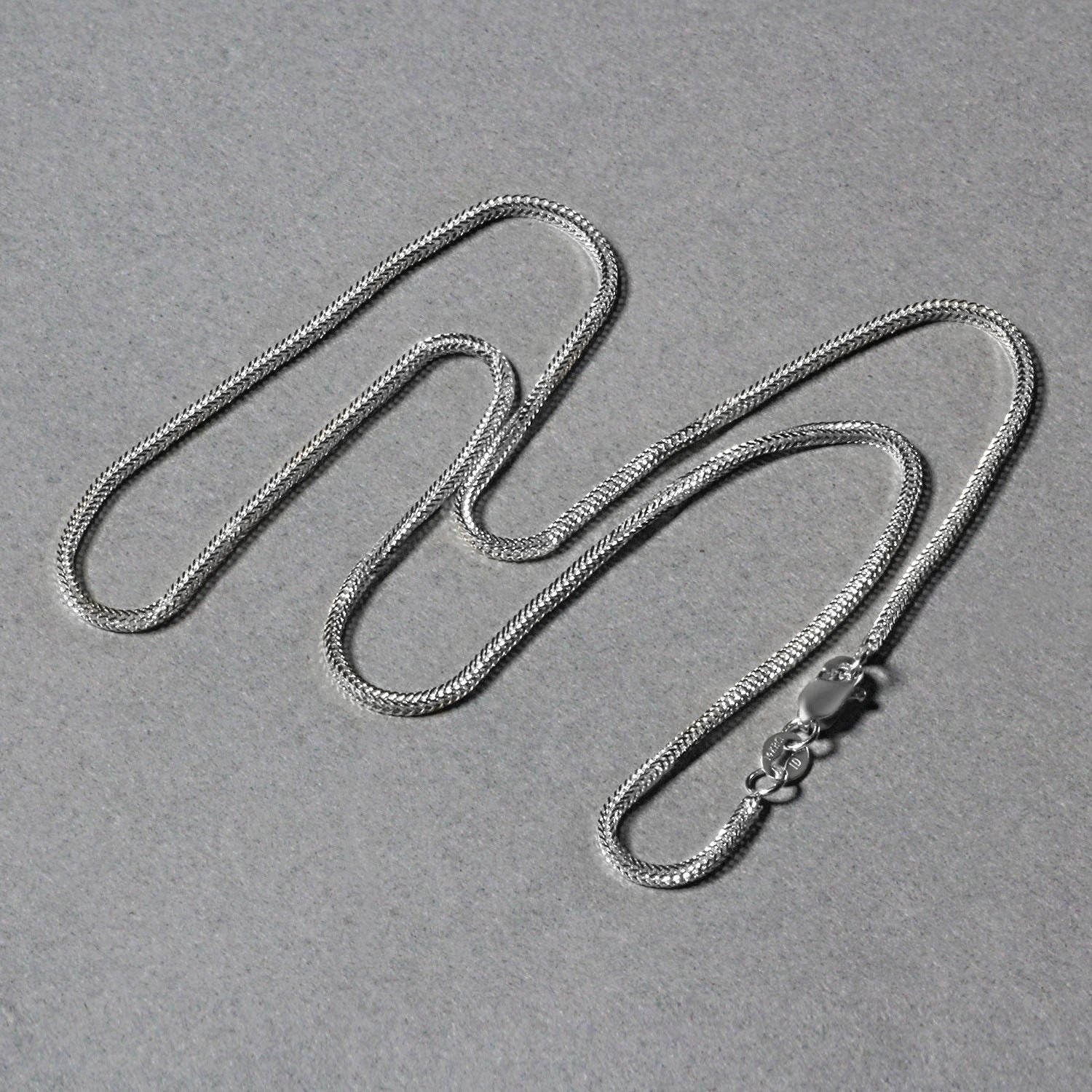 A 14k white gold foxtail chain with a lobster clasp lies on a gray surface.