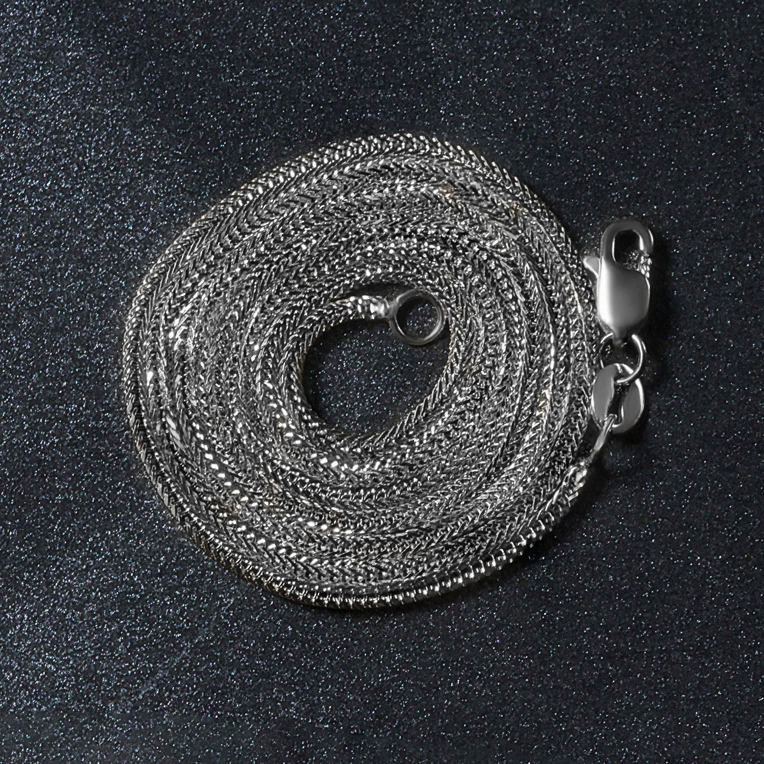 A coiled 14k white gold foxtail chain with a lobster clasp on a dark, glittery surface.
