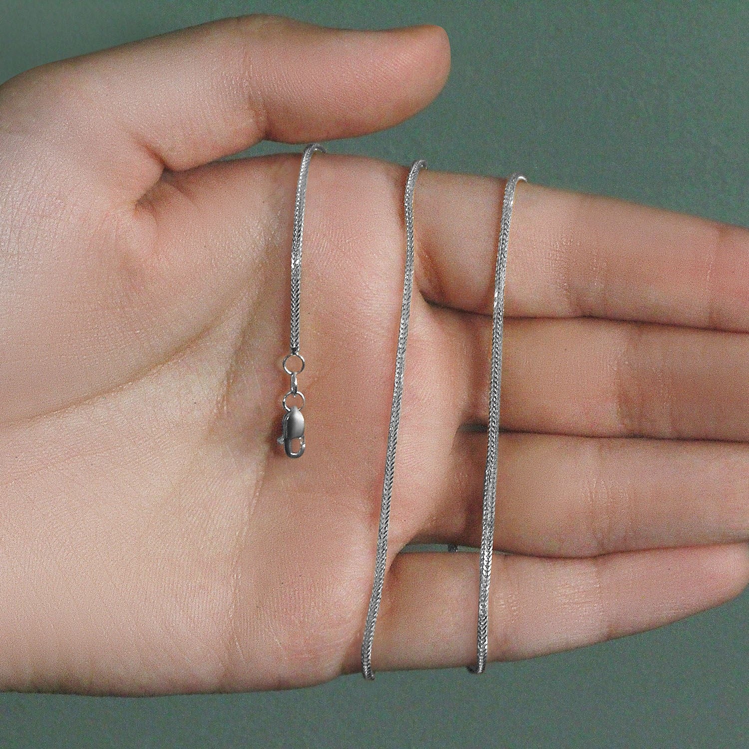 A 14k white gold foxtail chain with a lobster clasp is held across a person's palm.