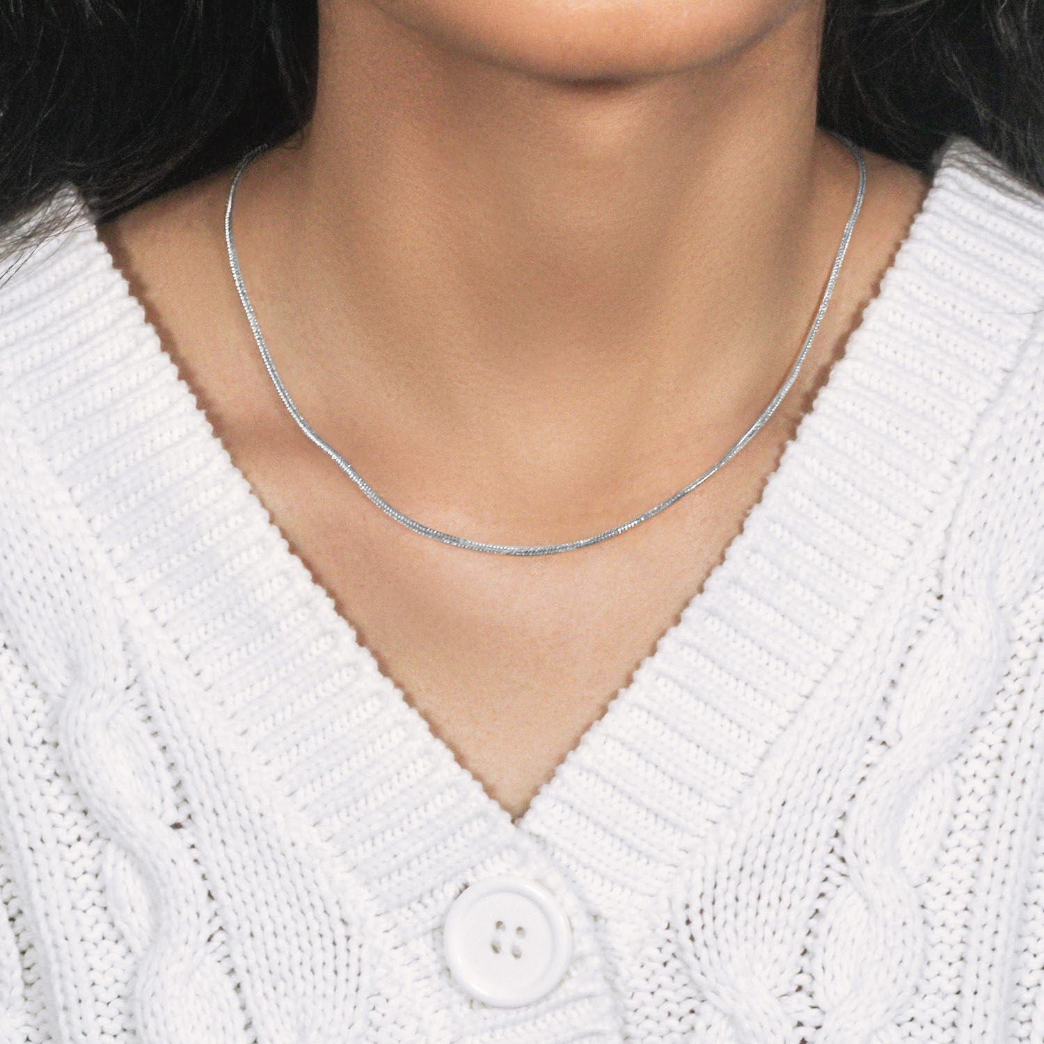 A 14k white gold foxtail chain with a lobster clasp is worn around a person's neck.