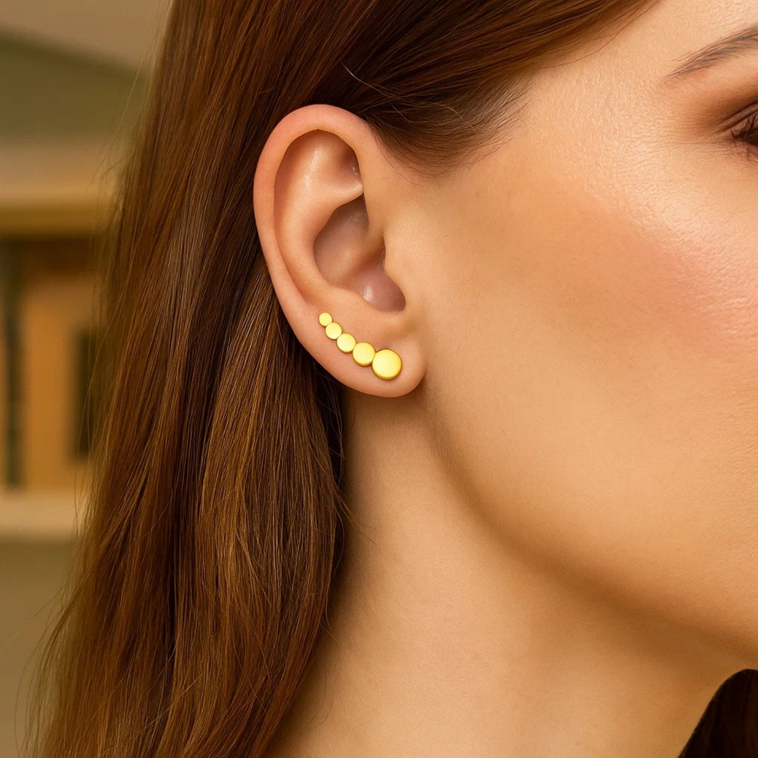 14k yellow gold graduated circles climber post earrings on a woman's ear.