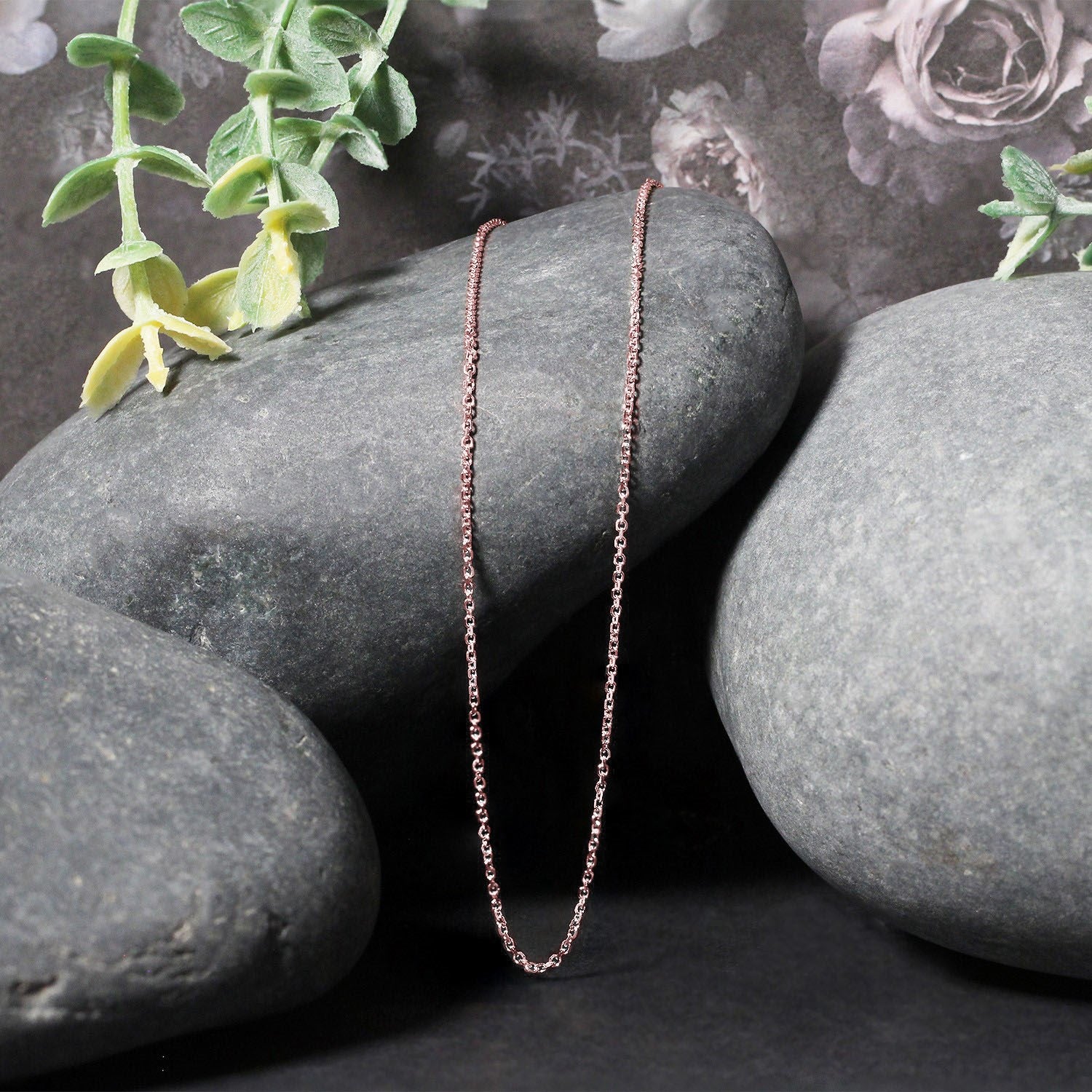 14k rose gold diamond cut cable link chain draped over smooth gray stones.