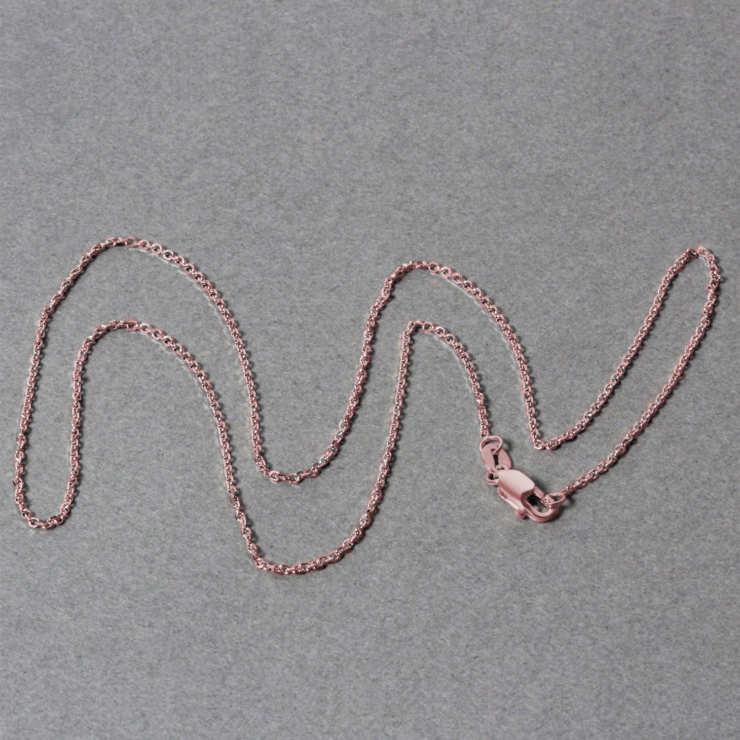 14k rose gold diamond cut cable link chain with a lobster clasp on a gray background.