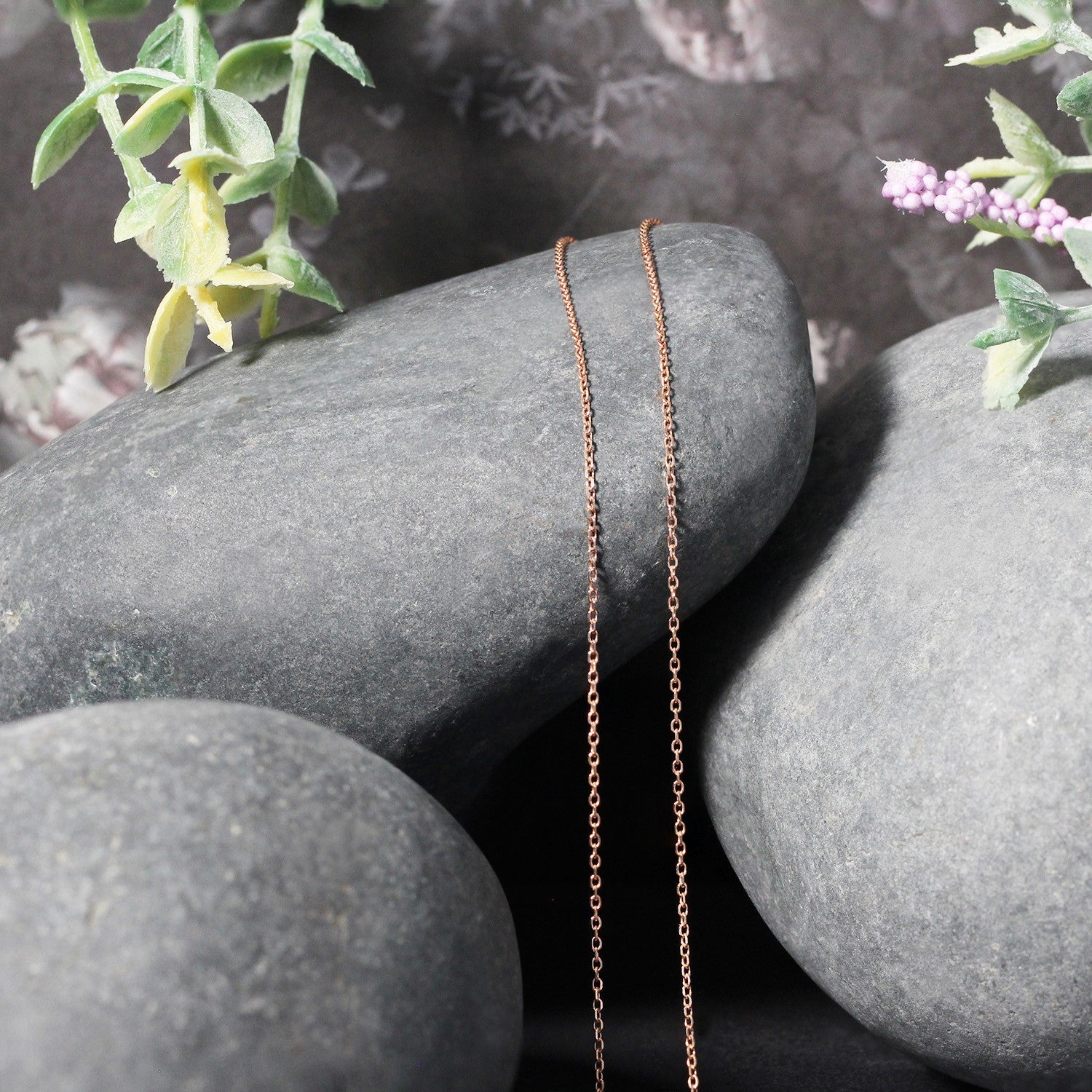 Rose gold diamond cut cable link chain draped over smooth gray stones.