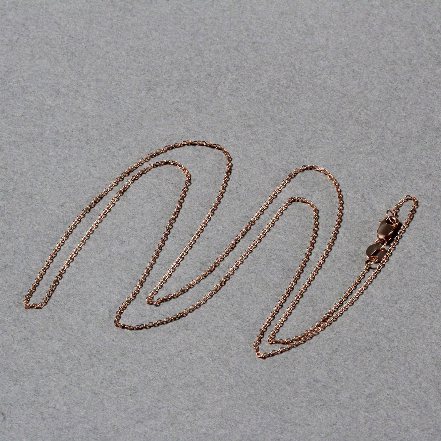 Rose gold diamond cut cable link chain with a lobster clasp on a gray background.