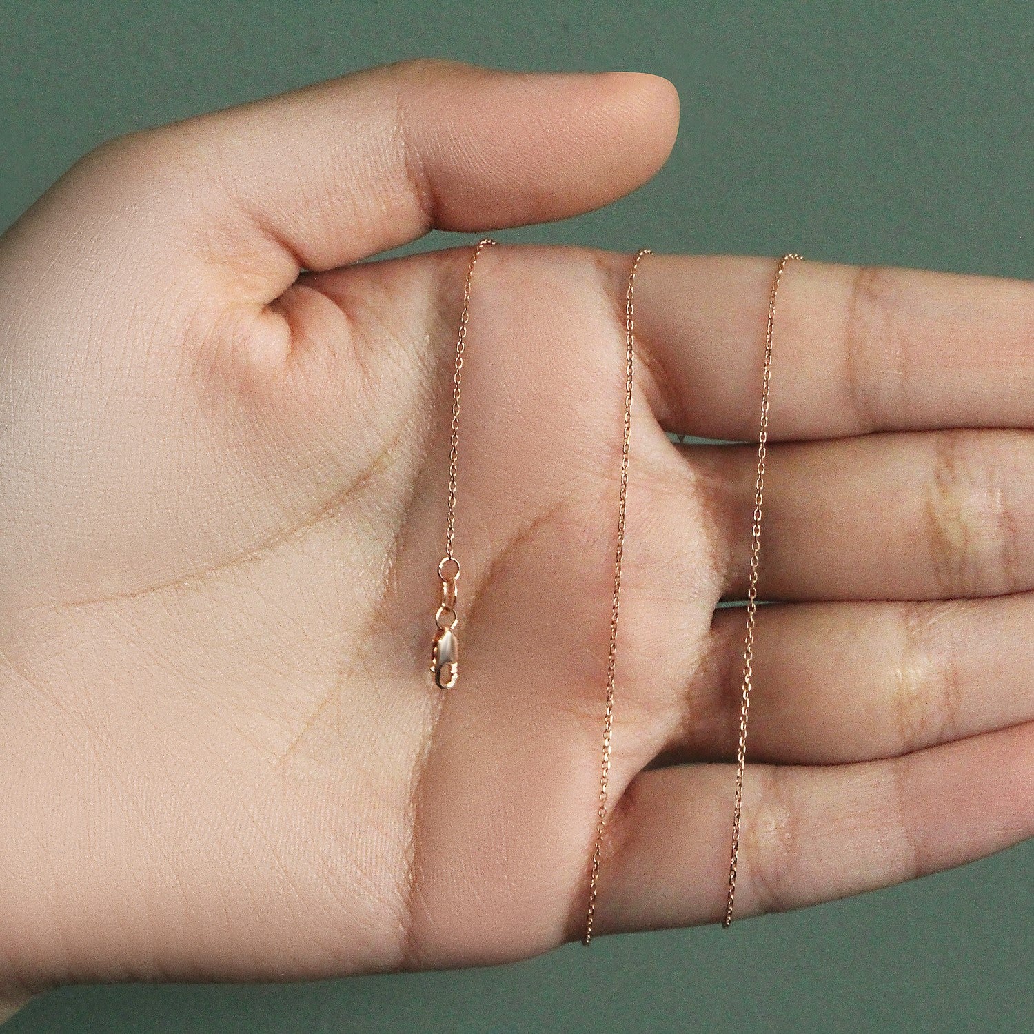 A rose gold diamond-cut cable link chain with a lobster clasp held in a hand.