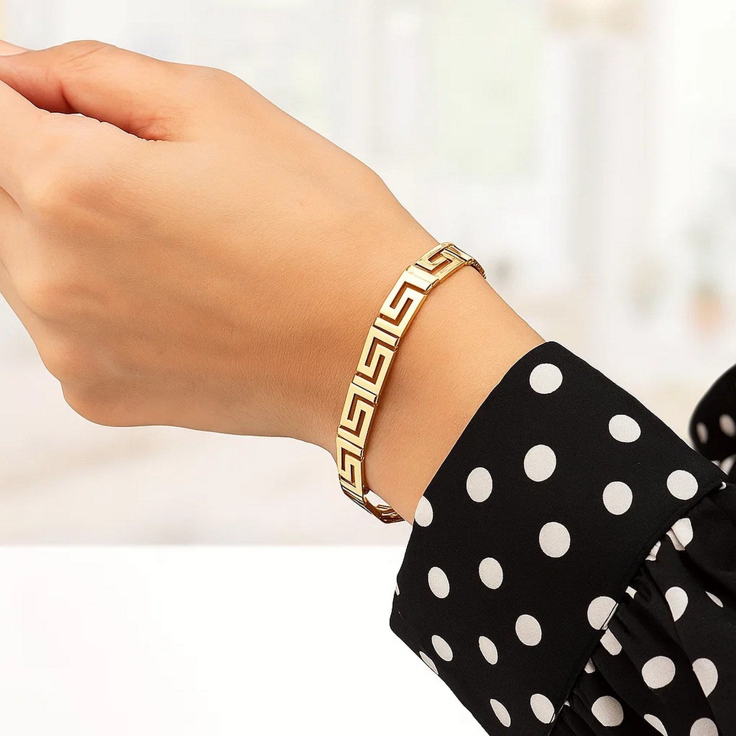 14k yellow gold bracelet with a Greek key motif on a person's wrist.
